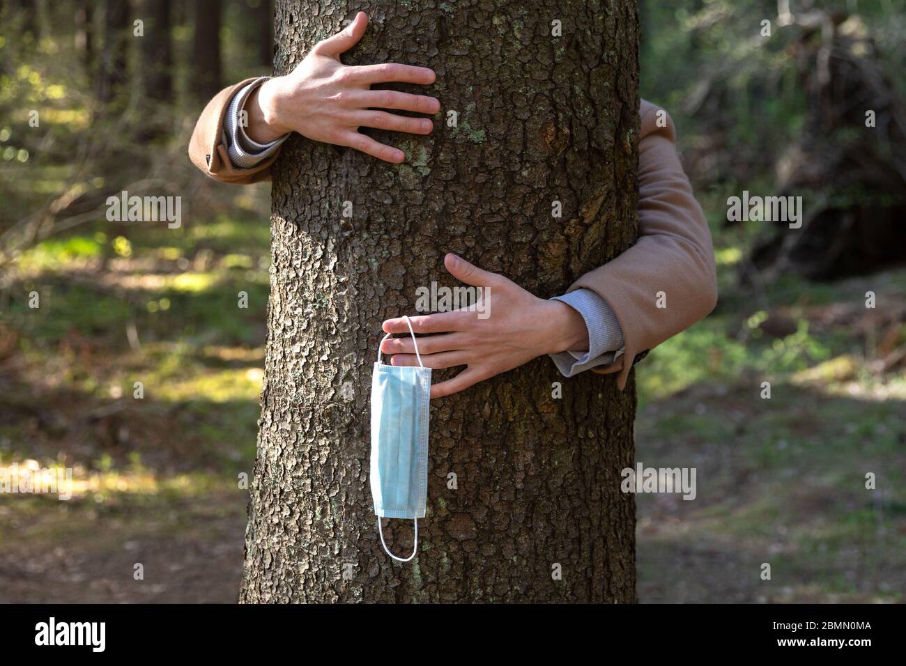 Primo piano delle mani che abbracciano un albero e toglie la maschera medica protettiva, lo tiene sulle sue dita, gode di vita, aria pulita fresca nella foresta dopo Co Foto Stock