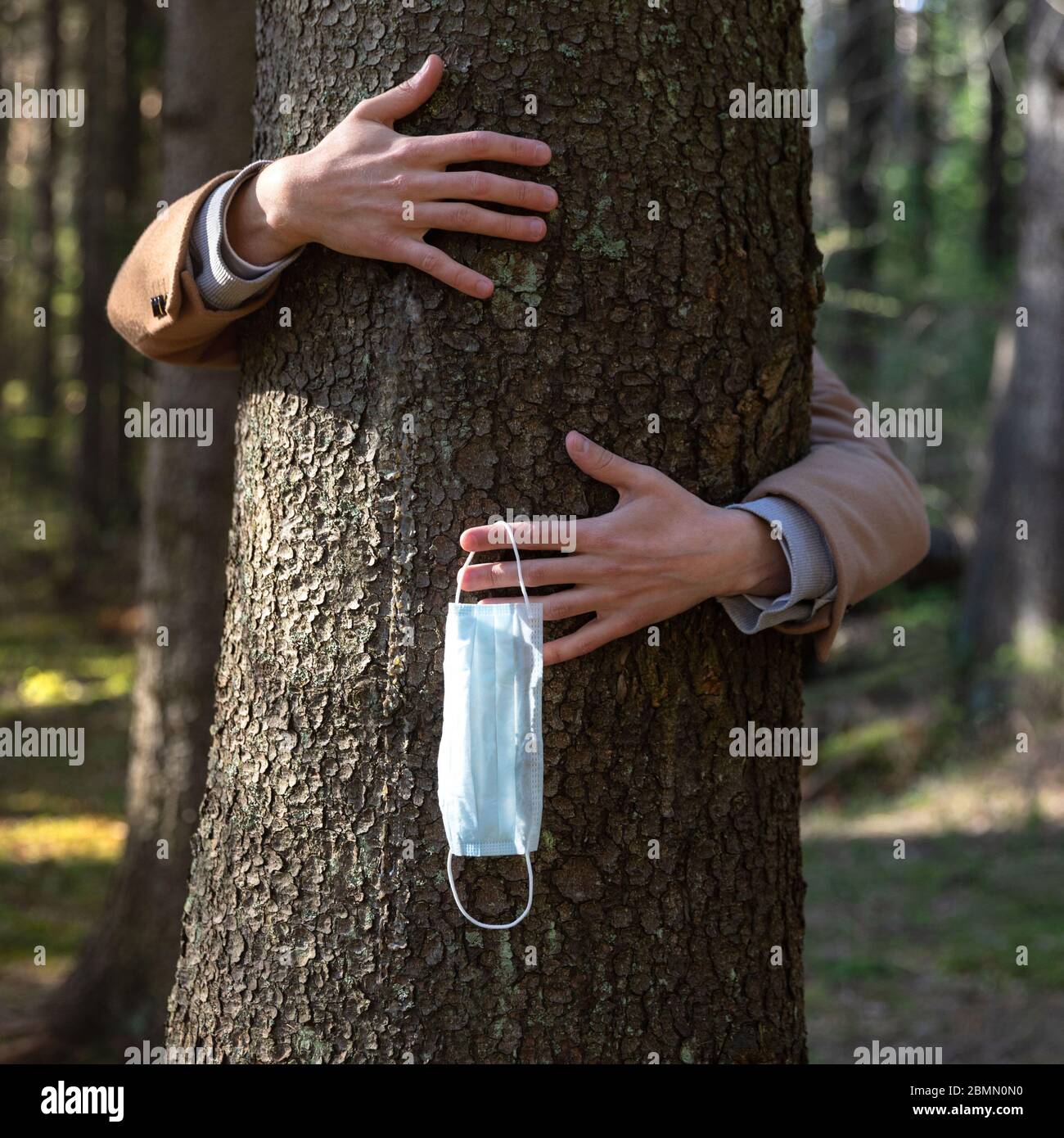 Primo piano delle mani che abbracciano un albero e toglie la maschera medica protettiva, lo tiene sulle sue dita, gode di vita, aria pulita fresca nella foresta dopo Co Foto Stock