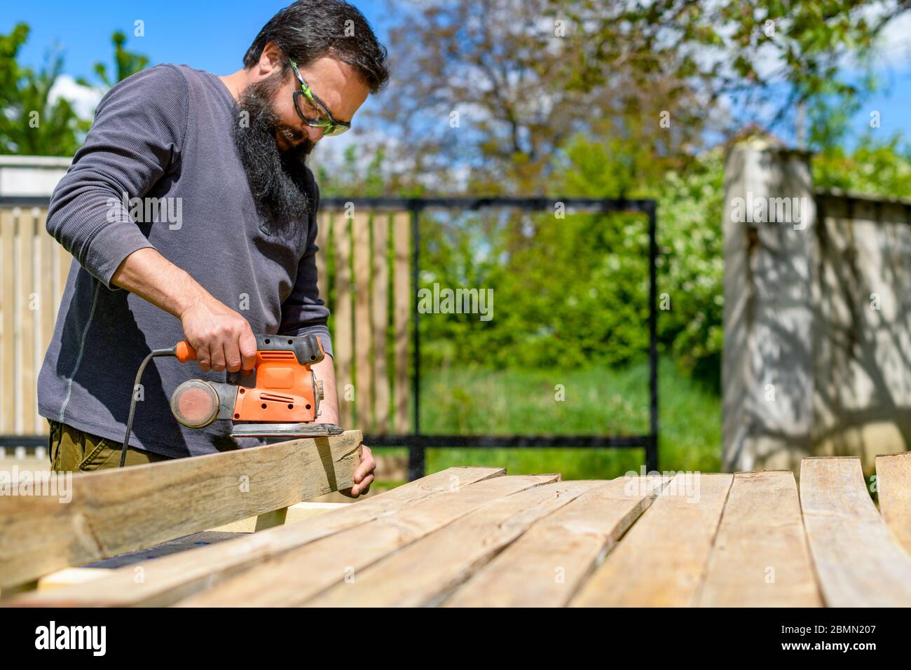 Uomo caucasico medio adulto nel giardino levigare tavole di legno. DIY miglioramento casa, restauro, Falegnameria concetto. Foto Stock