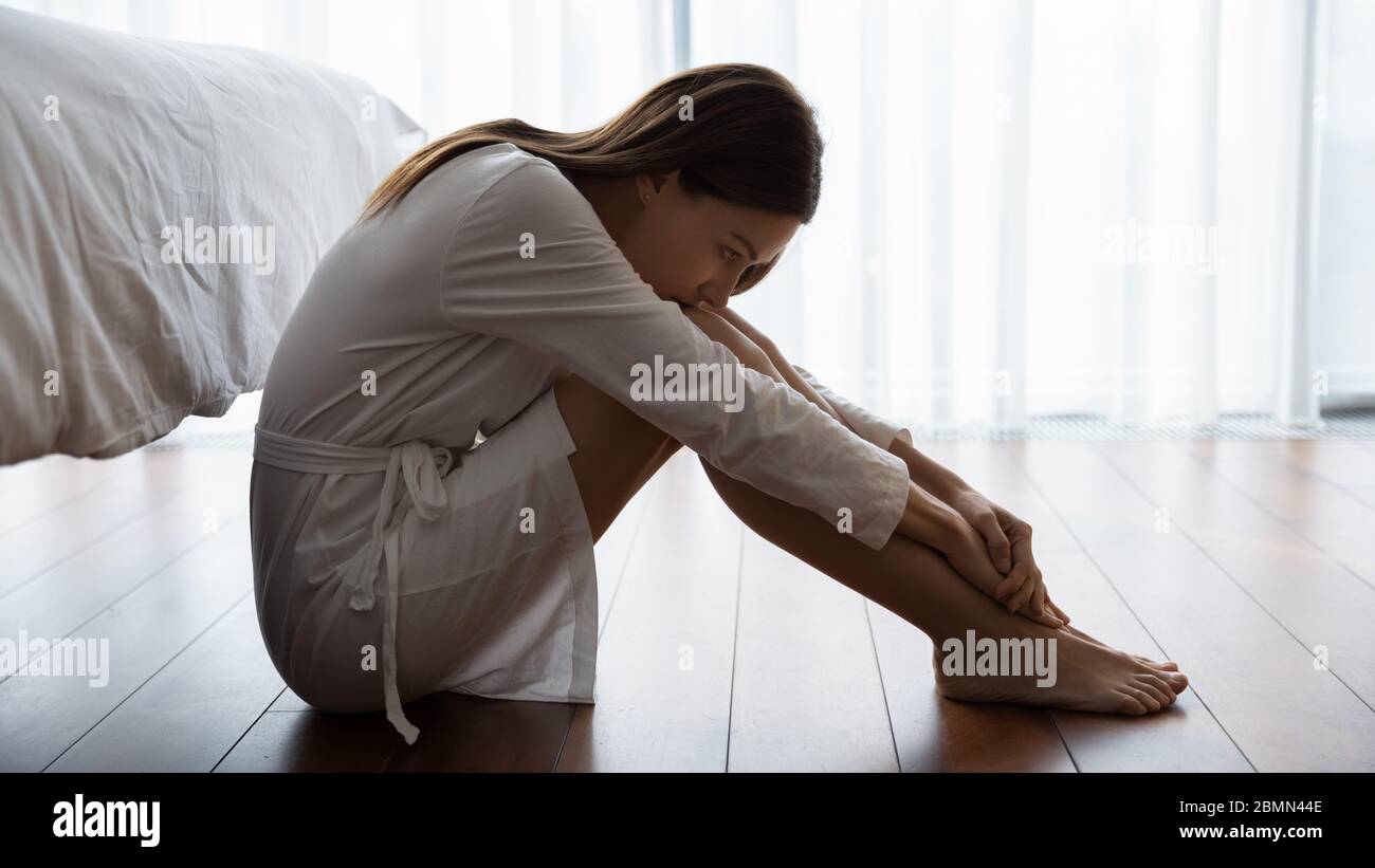 Donna triste seduta sul pavimento che osserva infelice soffre dalla solitudine Foto Stock