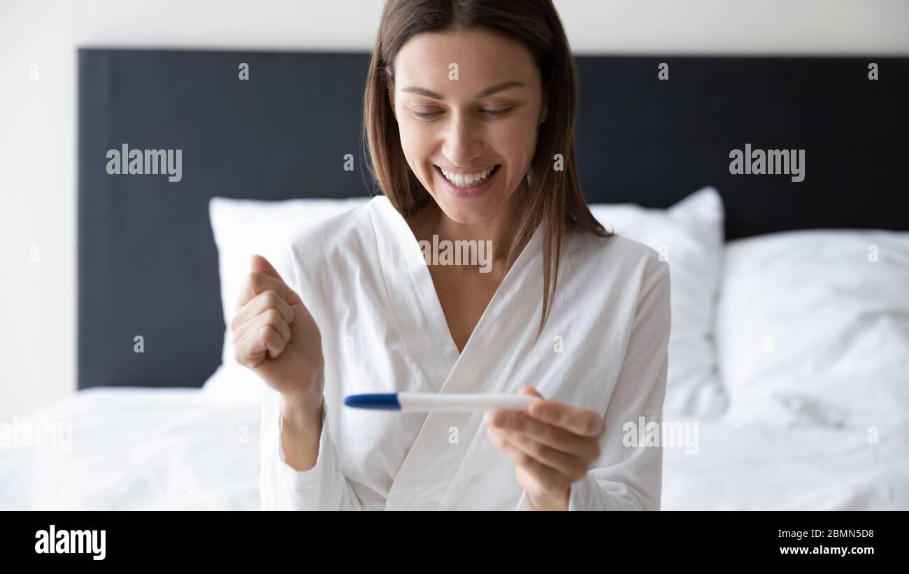 Donna che tiene il test di gravidanza concentrarsi sul viso felice eccitato Foto Stock