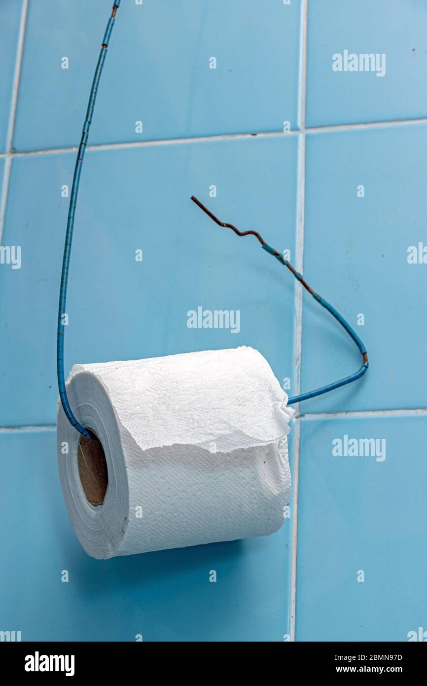 Un rotolo di carta igienica è appeso su un filo di una parete di piastrelle blu. Semplice porta carta igienica in bagno. Foto Stock