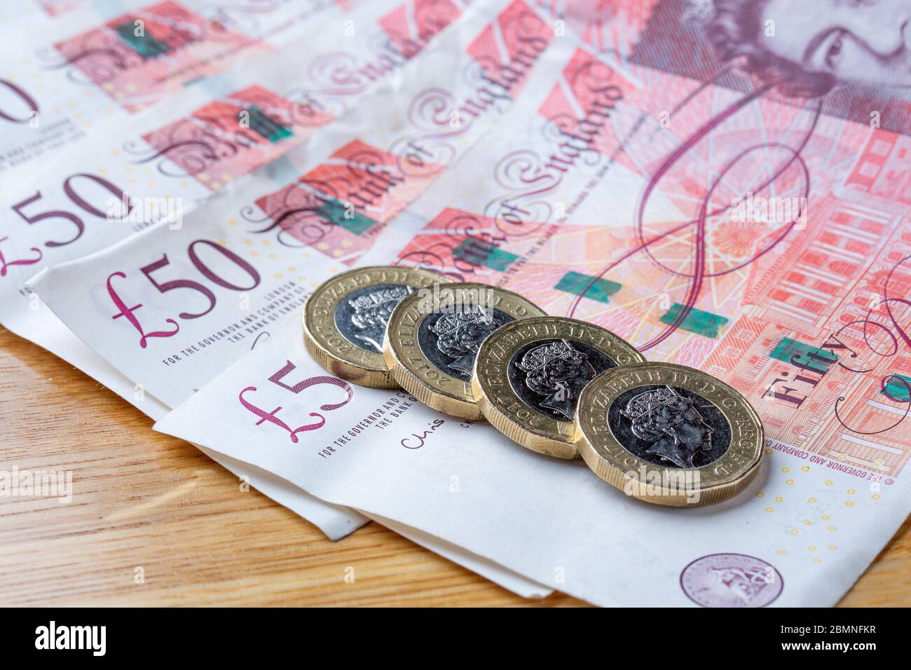 Monete da una libbra che si stendono su banconote da cinquanta libbre, monete da £1 e banconote da £50 inglesi Foto Stock