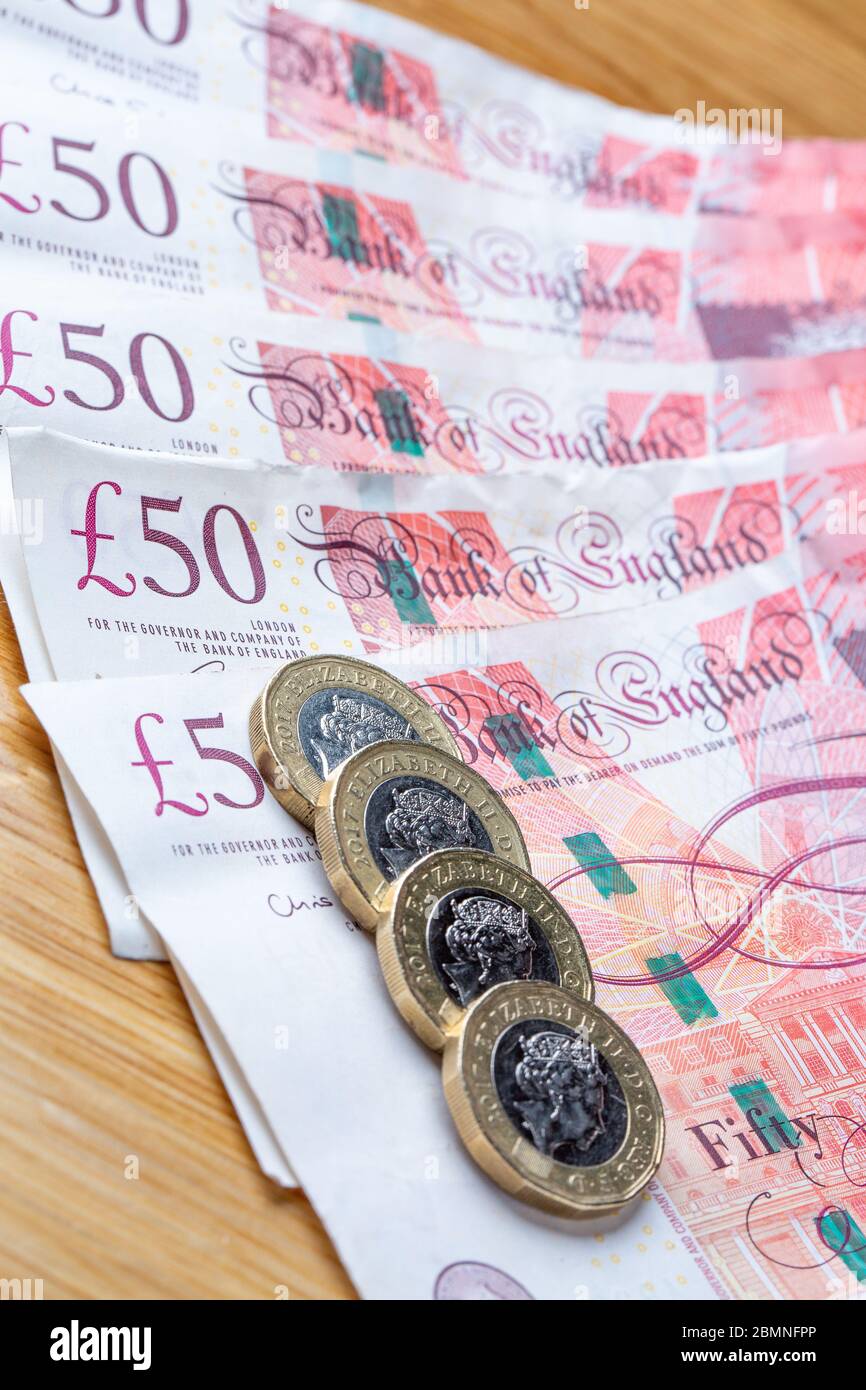 Monete da una libbra che si stendono su banconote da cinquanta libbre, monete da £1 e banconote da £50 inglesi Foto Stock