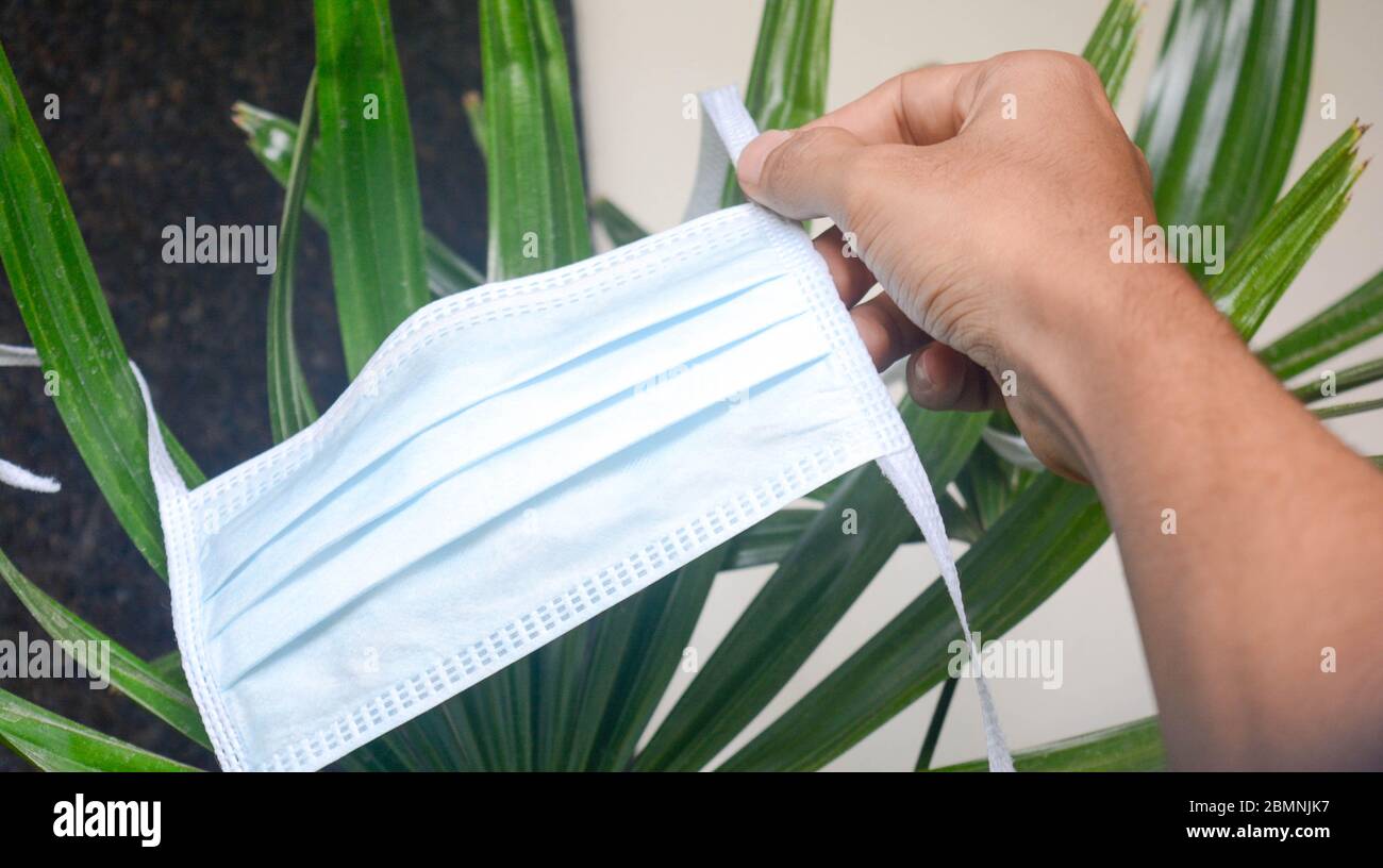 Uomo che tiene la maschera protettiva. Una maschera chirurgica su fondo pianta. Foto Stock