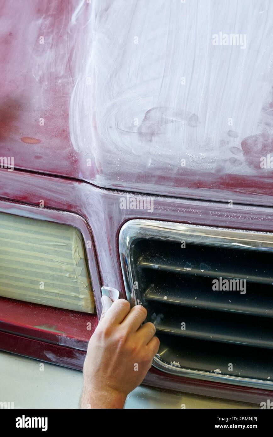 Una vista ravvicinata della mano di un uomo levigando il cofano di un camion prima di un lavoro di verniciatura Foto Stock