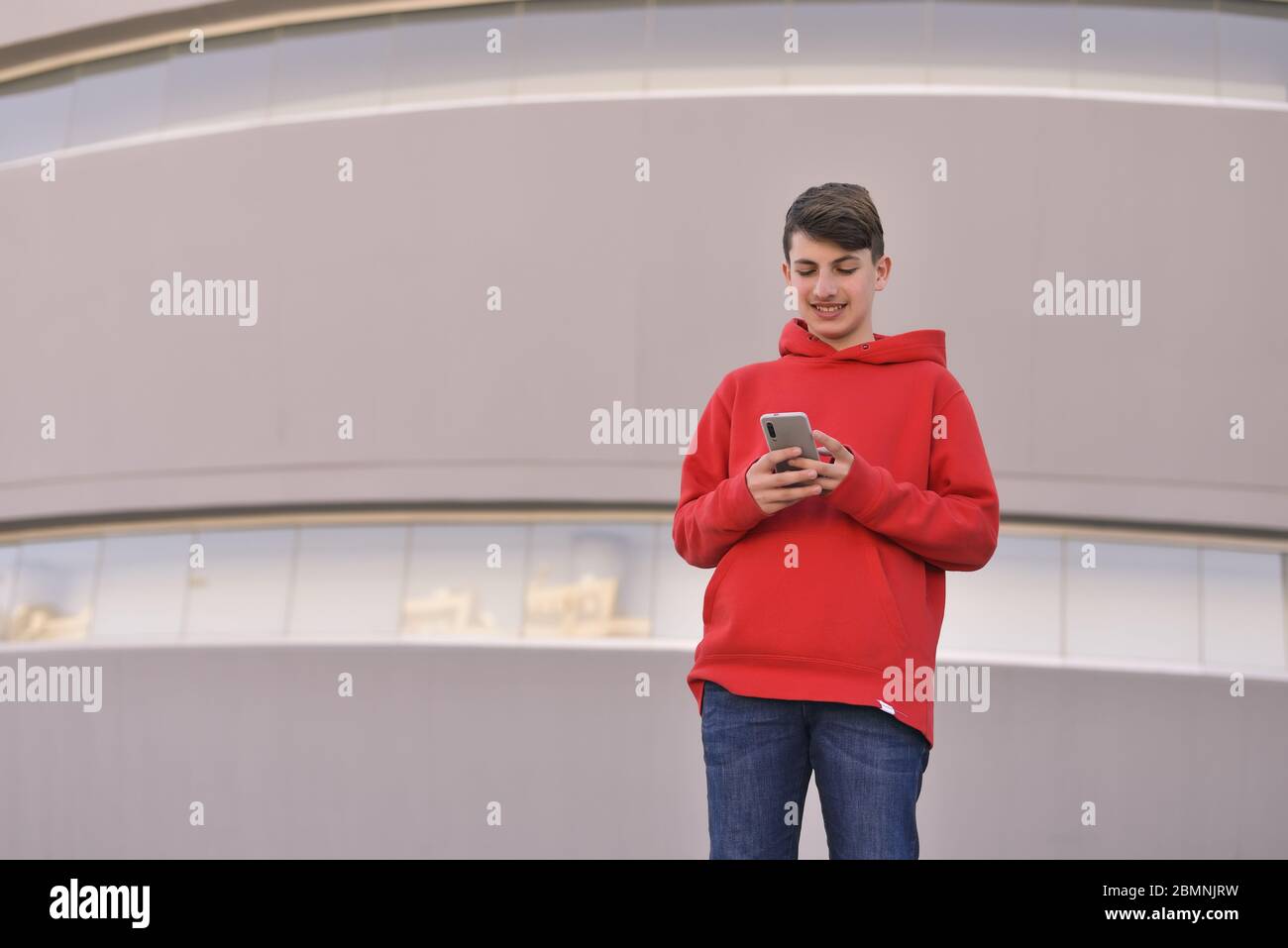 giovane uomo con abiti rossi alla porta del suo lavoro scrivendo un messaggio di testo con il suo smartphone Foto Stock