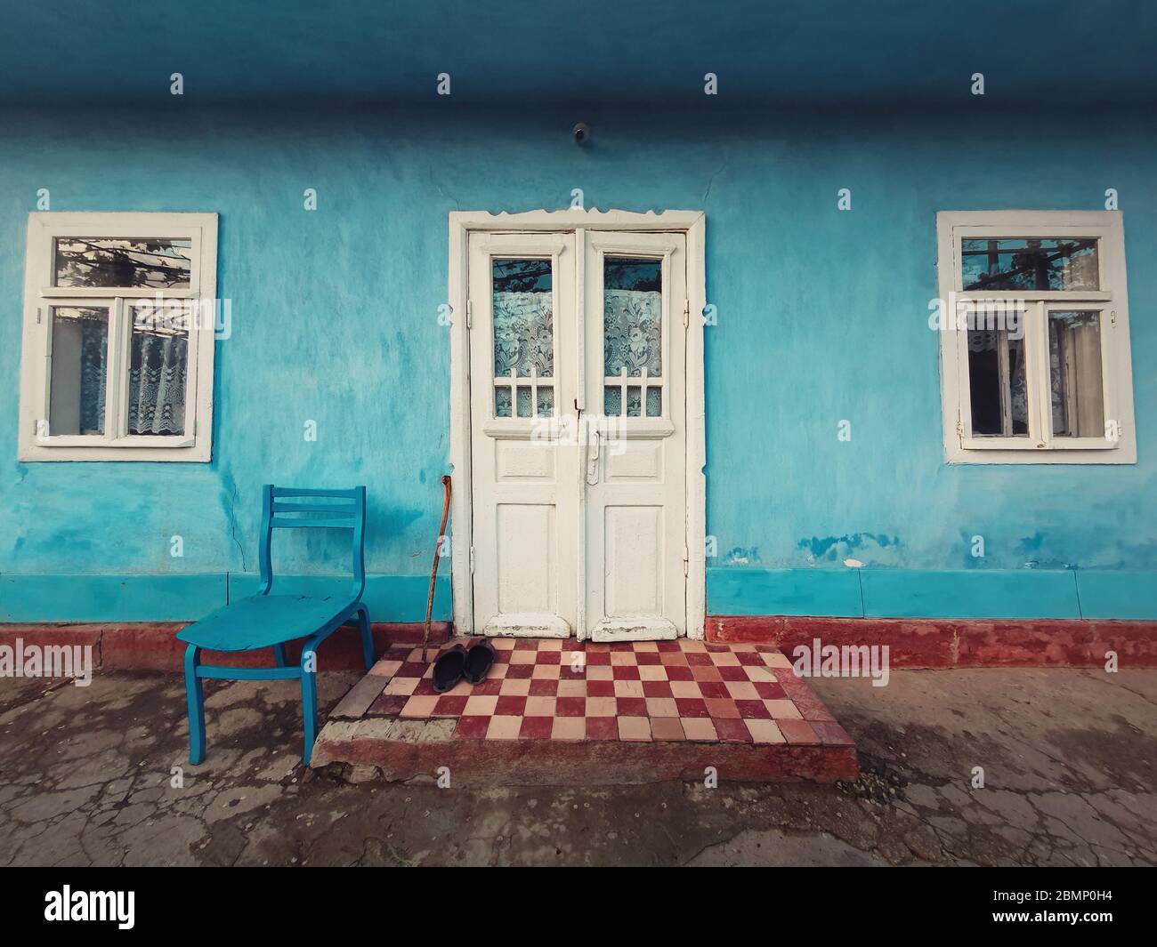 Bastone da passeggio, un paio di scarpe vecchie e una sedia a due passi di una casa vecchia. Tradizionale edificio rurale facciata. Pareti dipinte di calce blu, bianche Foto Stock