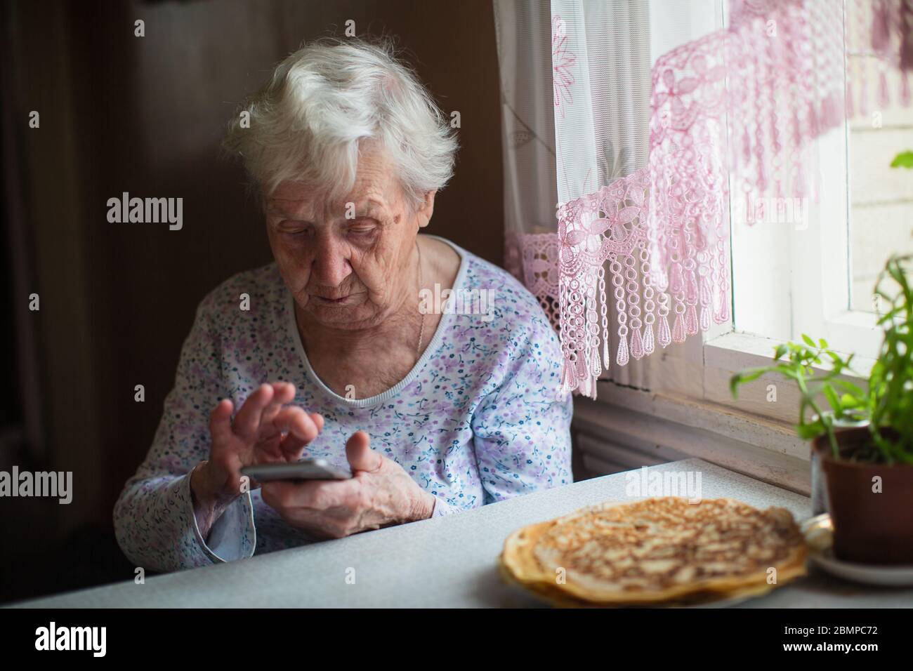 Autoisolamento dei pensionati. Una donna anziana siede con uno smartphone in mano a casa. Foto Stock