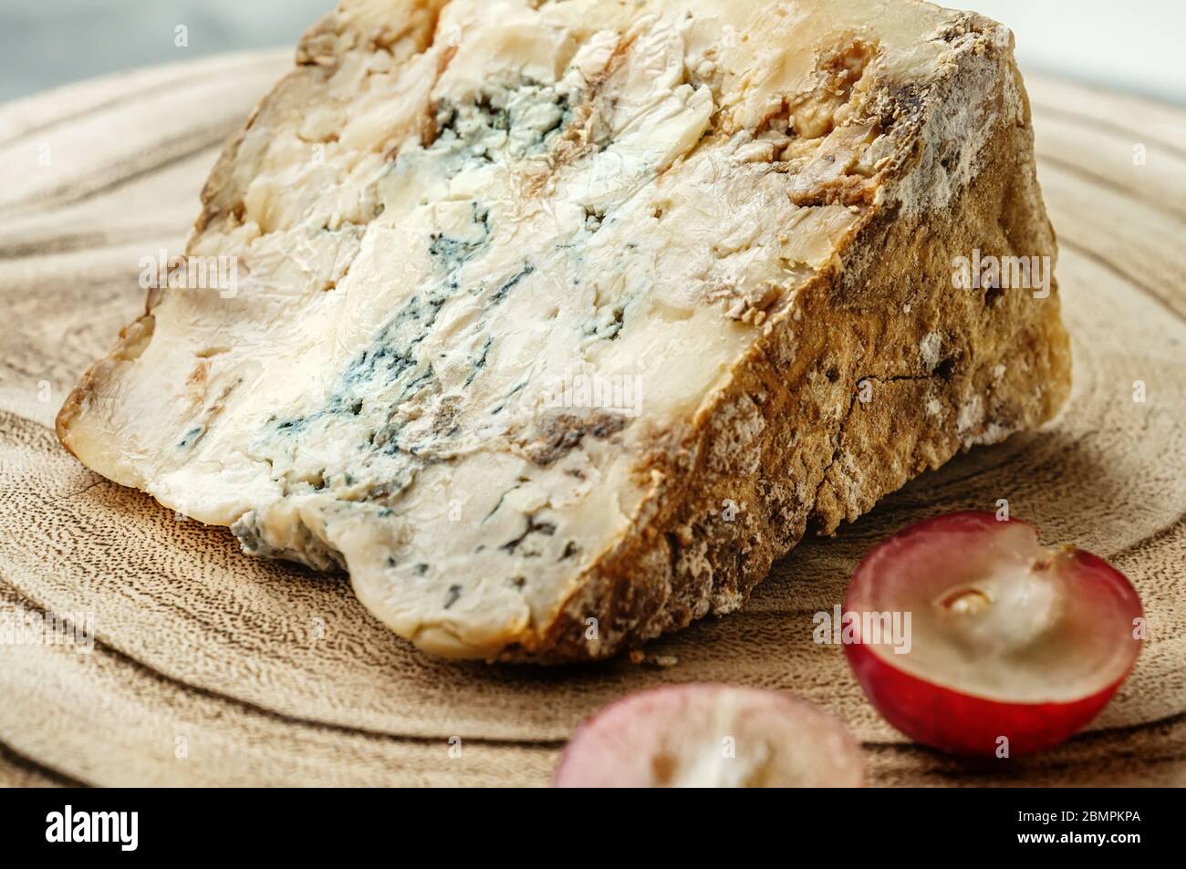 Un pezzo di formaggio Stilton blu su un antico sfondo ligneo con grandi uve rosse. Primo piano. Foto Stock