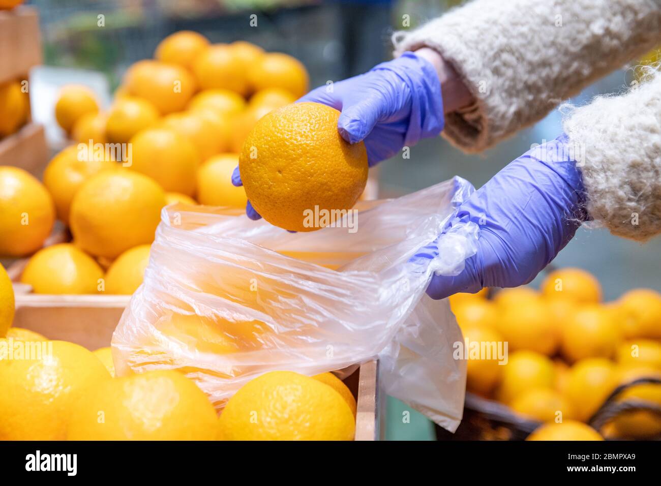 Donna mani in guanti medici sceglie arance fresche pieghevole in un sacchetto di plastica monouso in supermercato, primo piano. Misure di protezione contro i coronavi Foto Stock