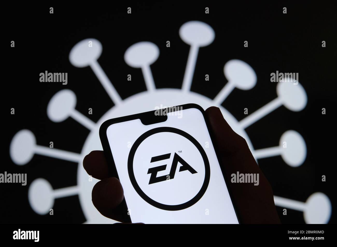 Il logo Electronic Arts (EA) sulla silhouette di uno smartphone è in mano. Immagine di coronavirus sullo sfondo sfocato. Foto reale, non un montaggio. Foto Stock