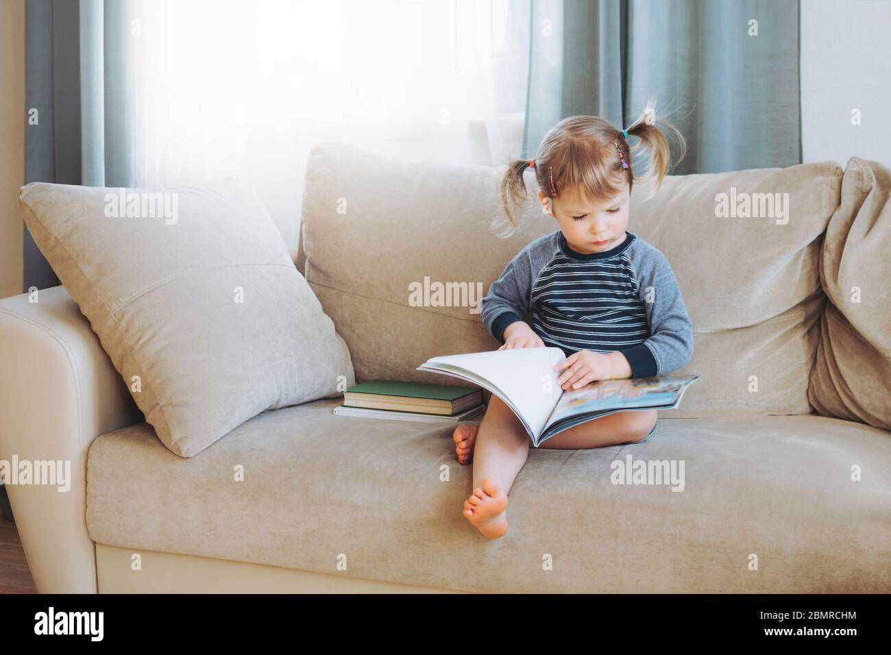 Bambina che legge un libro a casa sul divano. Formazione a distanza. Detox digitale. Foto Stock