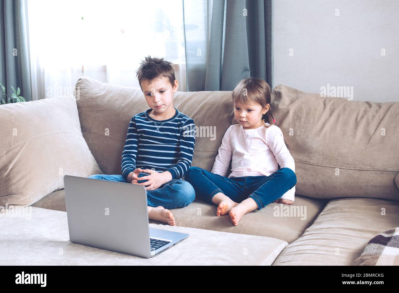 I bambini studiano a casa utilizzando lezioni online sul divano, guardando cartoni animati online. Quarantena a casa. Formazione a distanza, formazione online. Foto Stock