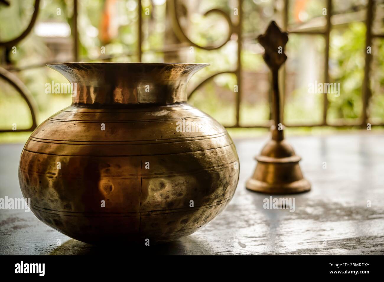 Primo piano Still Life of Antique Holi Water pot e campana su pavimento rustico. Fede, tradizione, spiritualità, preghiera, simboli di pace e temi religiosi. Foto Stock
