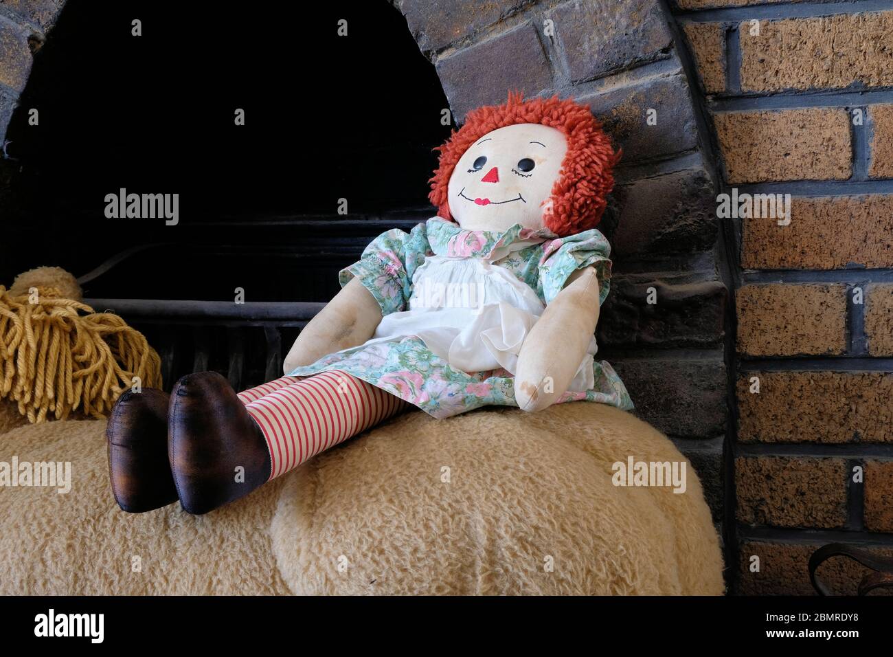 Bambola Raggedy Ann seduta accanto a un caminetto all'interno di una casa; bambola straccio. Foto Stock