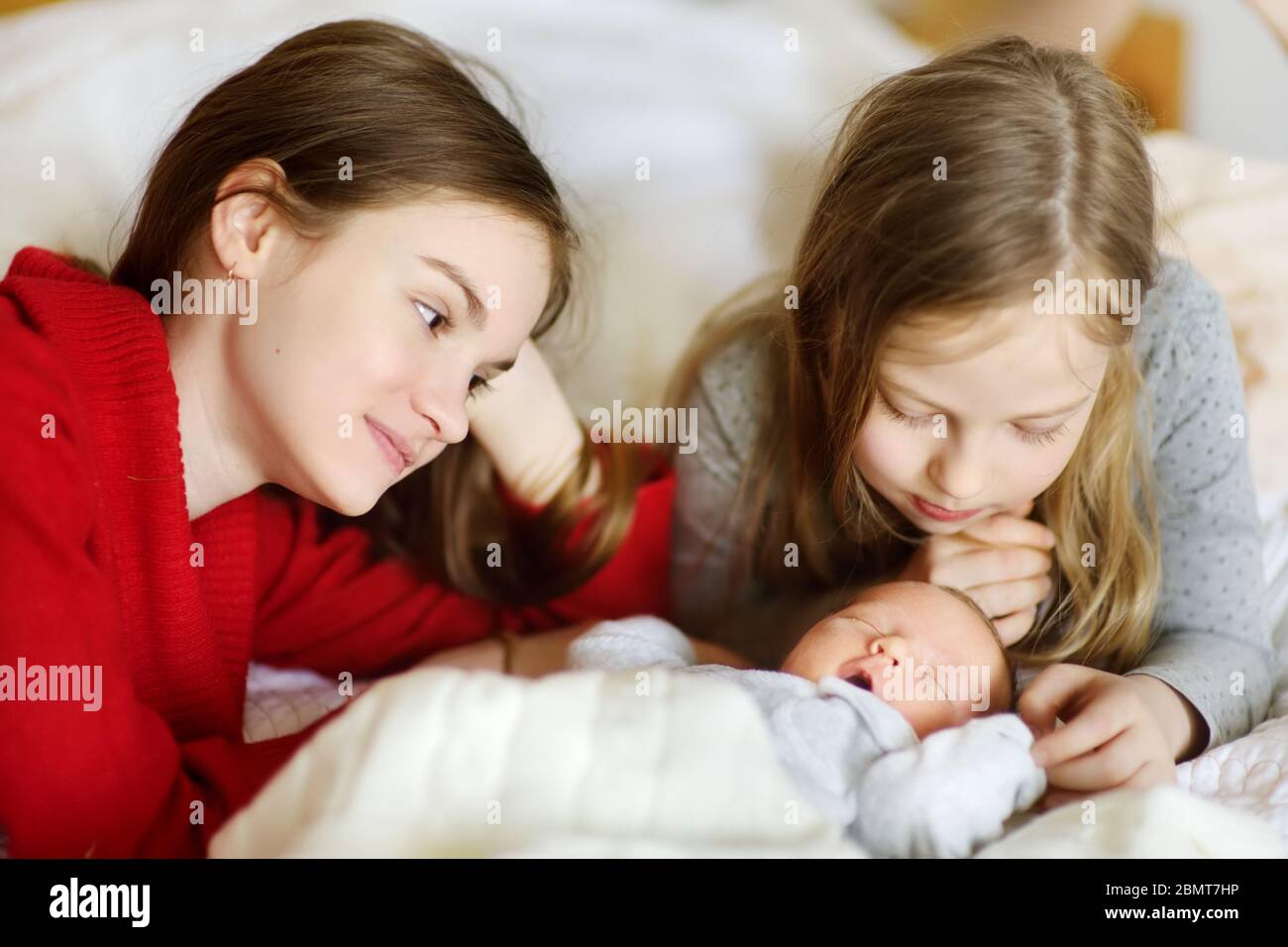 Due grandi sorelle ammirano il loro fratello neonato che dormiva. Due ragazze che tengono il loro nuovo bambino ragazzo. Bambini con grande spazio per età. Grande differenza di età betwe Foto Stock