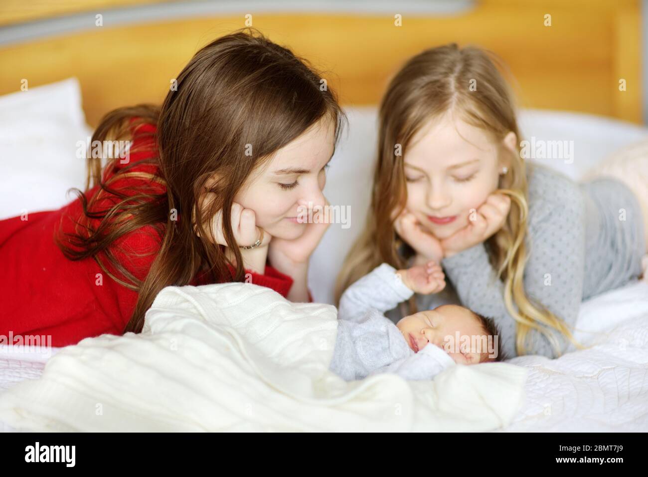 Due grandi sorelle ammirano il loro fratello neonato che dormiva. Due ragazze che tengono il loro nuovo bambino ragazzo. Bambini con grande spazio per età. Grande differenza di età betwe Foto Stock