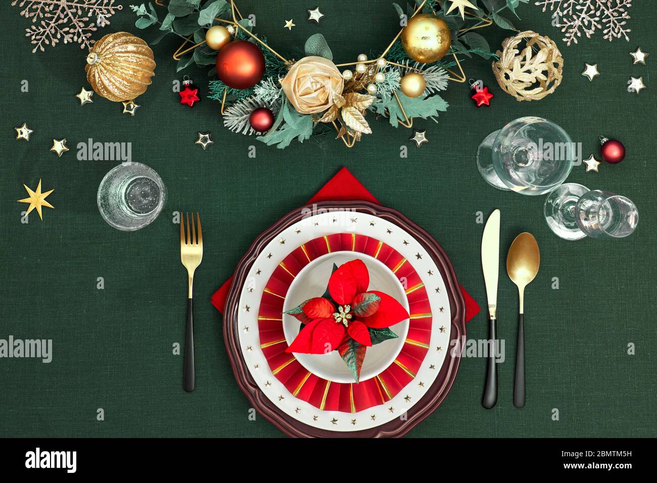 Tavola di Natale messa a punto con piatti rossi bianchi scuri, anello di carta rosso e poinsettia, utensili d'oro. Decorazioni dorate rosse, verdi e dorate. Disposizione piatta, Foto Stock