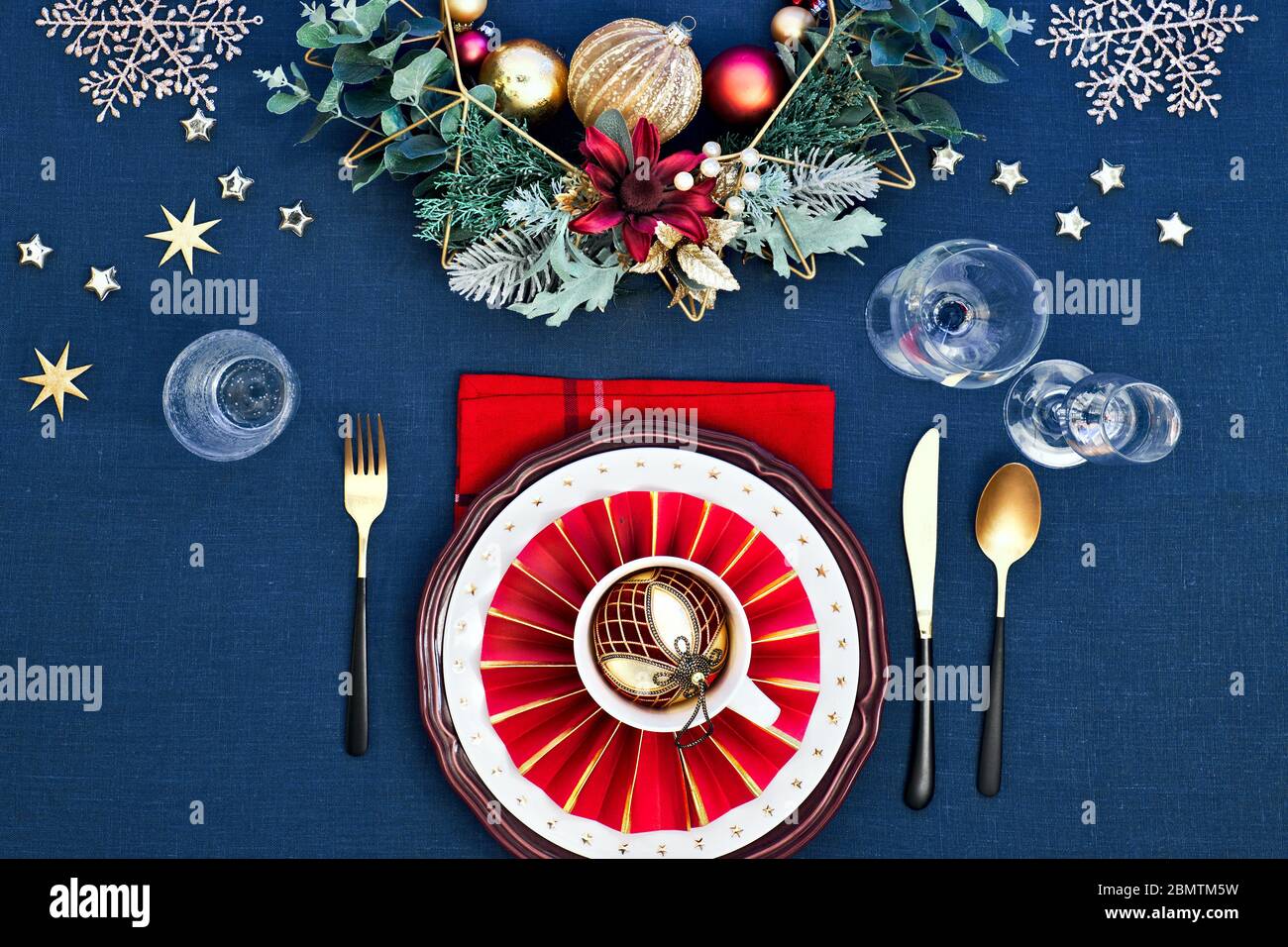 Tavola di Natale messa a punto con piatti rossi bianchi scuri, anello di carta rosso e poinsettia, utensili d'oro. Decorazioni dorate rosse, verdi e dorate. Disposizione piatta, Foto Stock