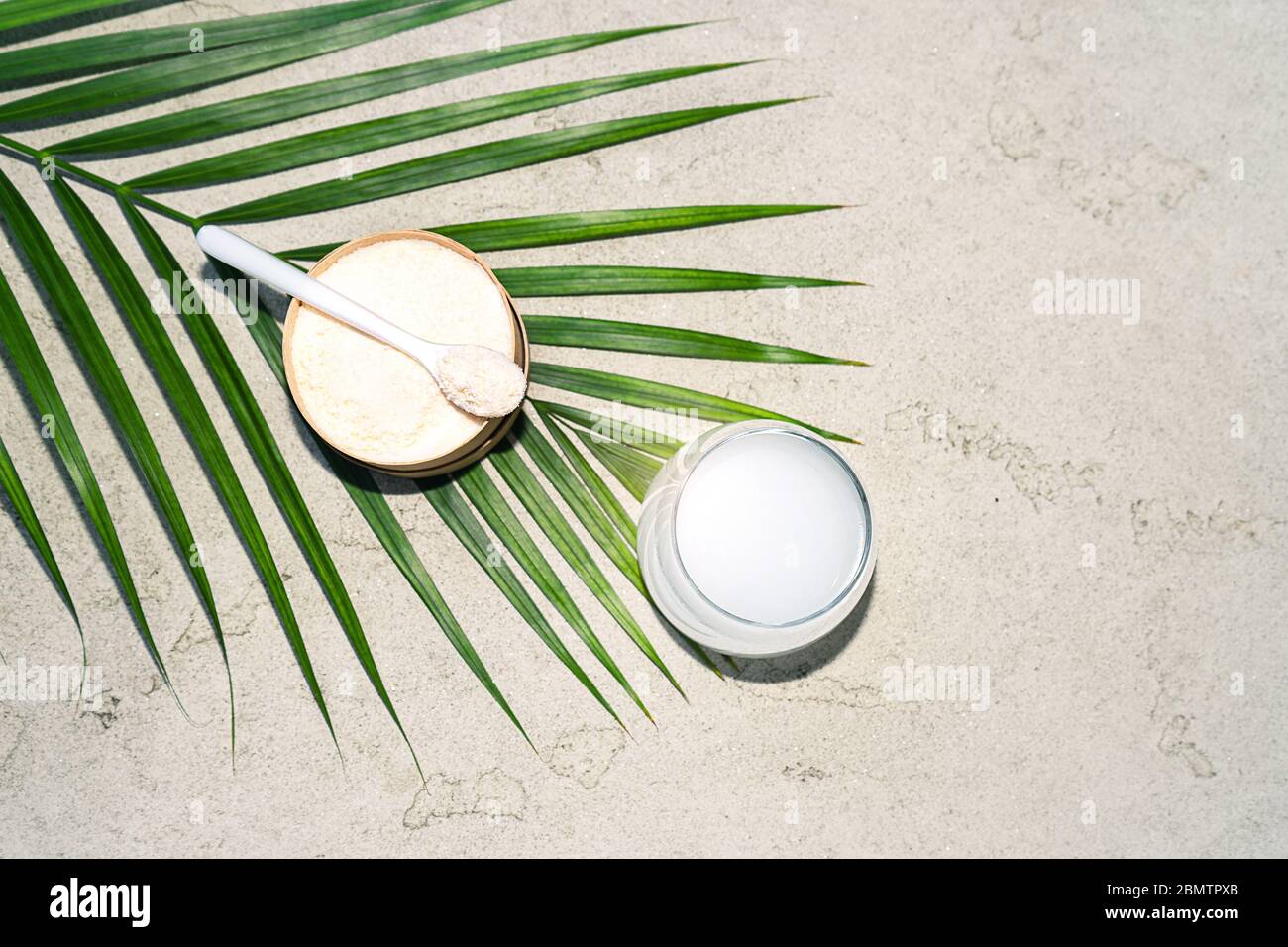 Collagene con cucchiaio e bicchiere d'acqua su fondo in cemento. Concetto di salute e bellezza alla moda. Foto Stock