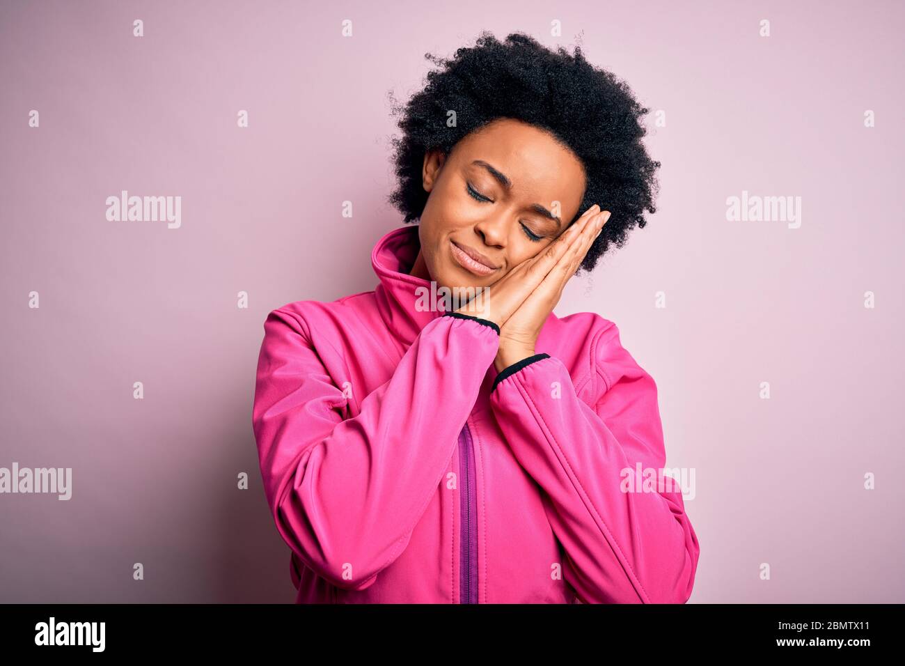 Giovane afro sportivo afro americano giovane con capelli ricci indossare abbigliamento sportivo doin sport dormire stanco sognare e posare con le mani insieme mentre smi Foto Stock