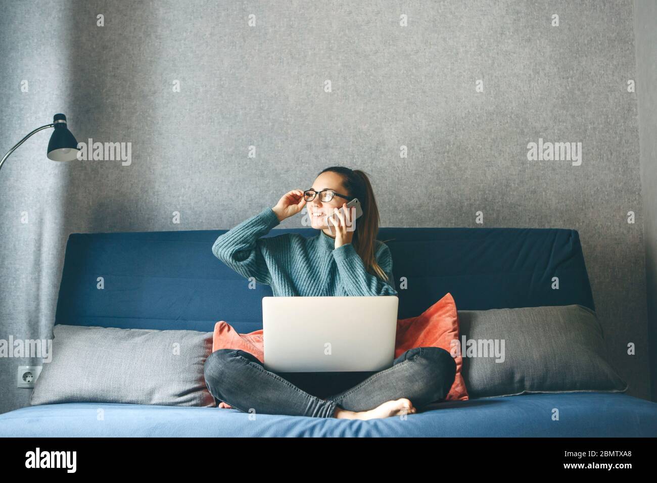 Una ragazza lavora da casa o uno studente sta studiando da casa o da un freelancer. Utilizza un computer portatile e un telefono. Foto Stock