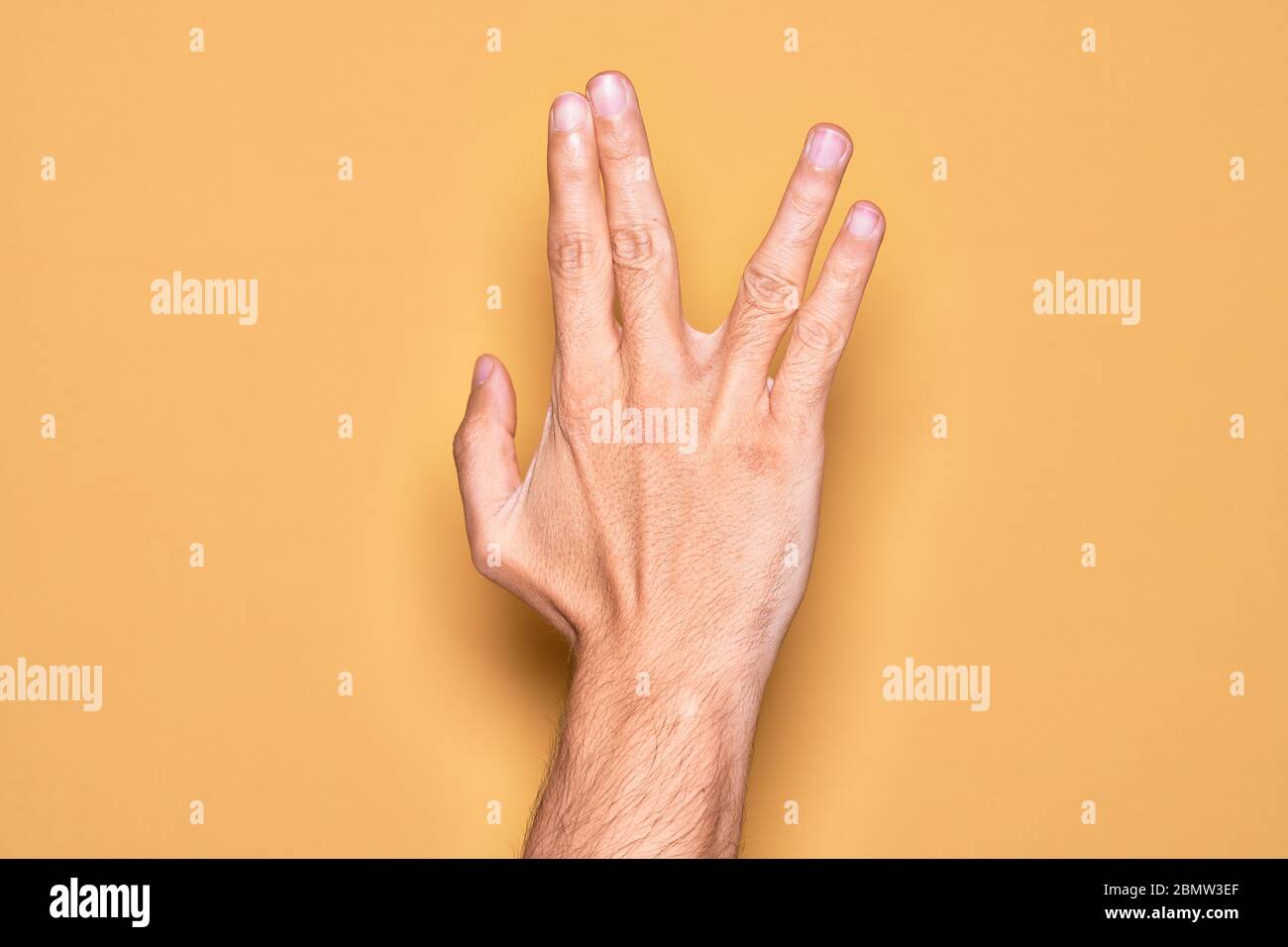 Mano di giovane caucasico che mostra le dita sopra isolato sfondo giallo saluto facendo Vulcan salutare, mostrando la parte posteriore della mano e le dita, freak Foto Stock