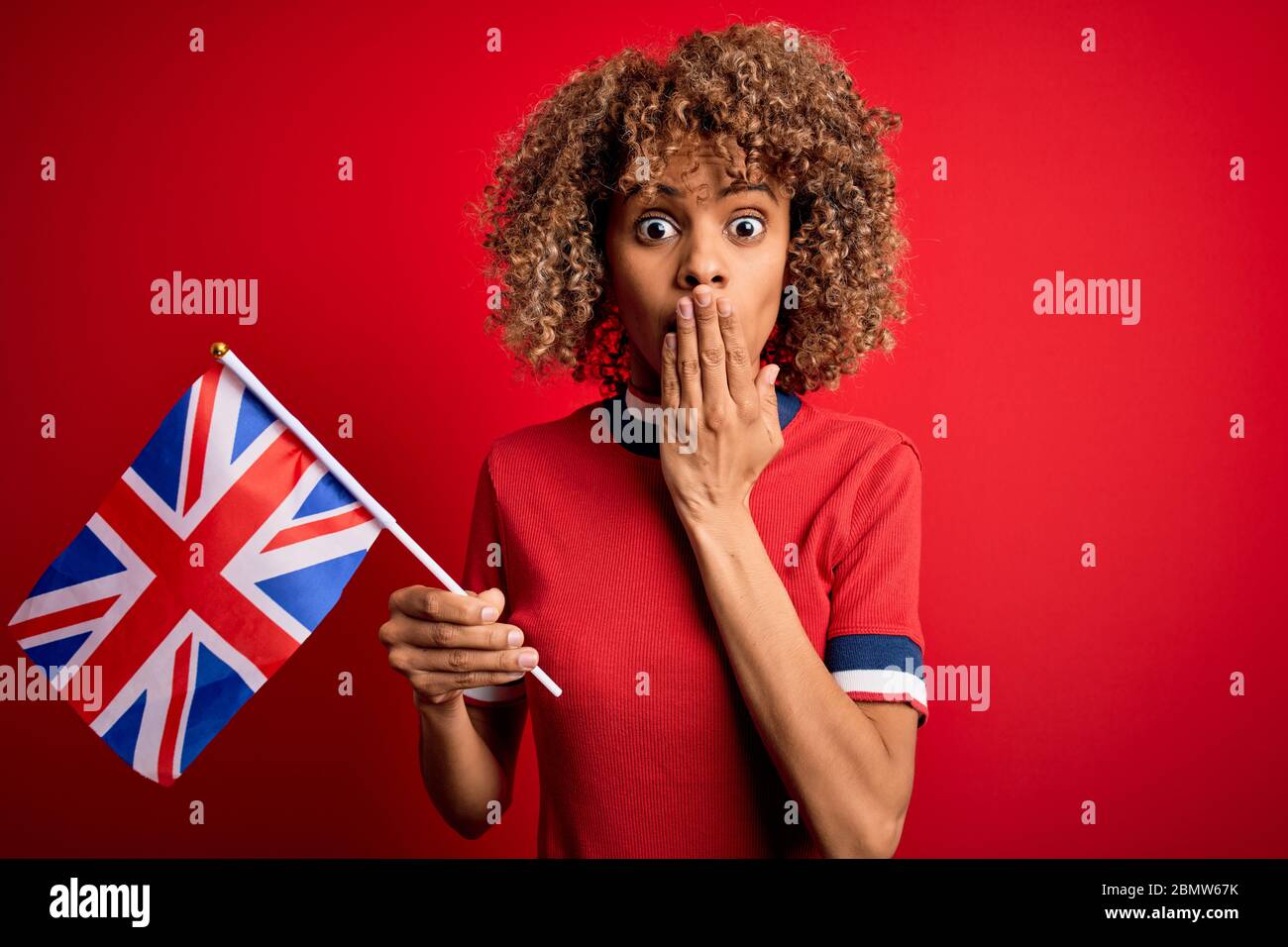 Giovane maledetta afro-americana che tiene la bandiera britannica per celebrare il referendum sulla brexit coprire la bocca con la mano scioccata con vergogna per errore, espressione di f Foto Stock