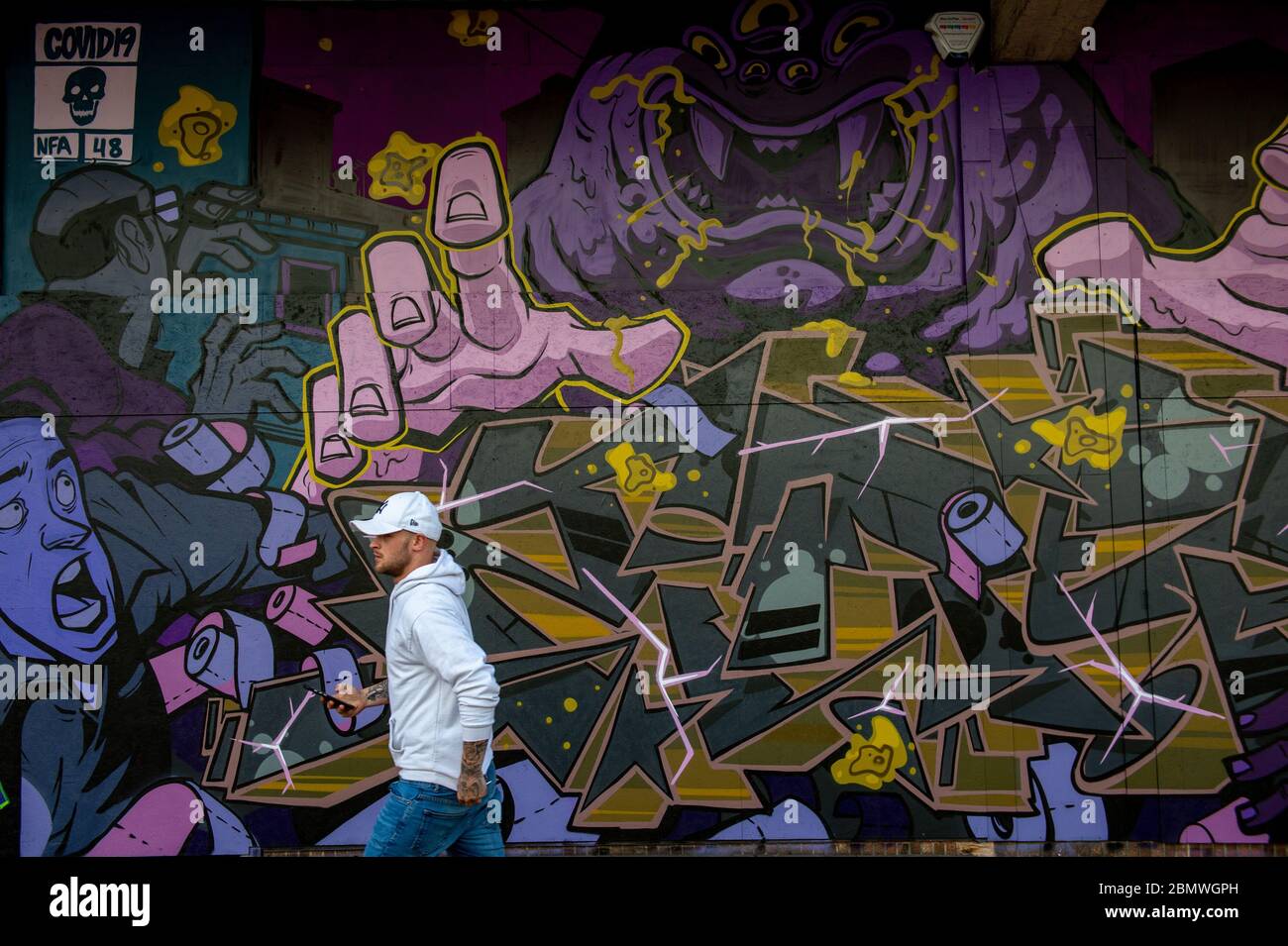 Un uomo cammina con graffiti a tema coronavirus nel centro di Birmingham, mentre il Regno Unito continua a fare il lock-down per contribuire a frenare la diffusione del coronavirus. Foto Stock