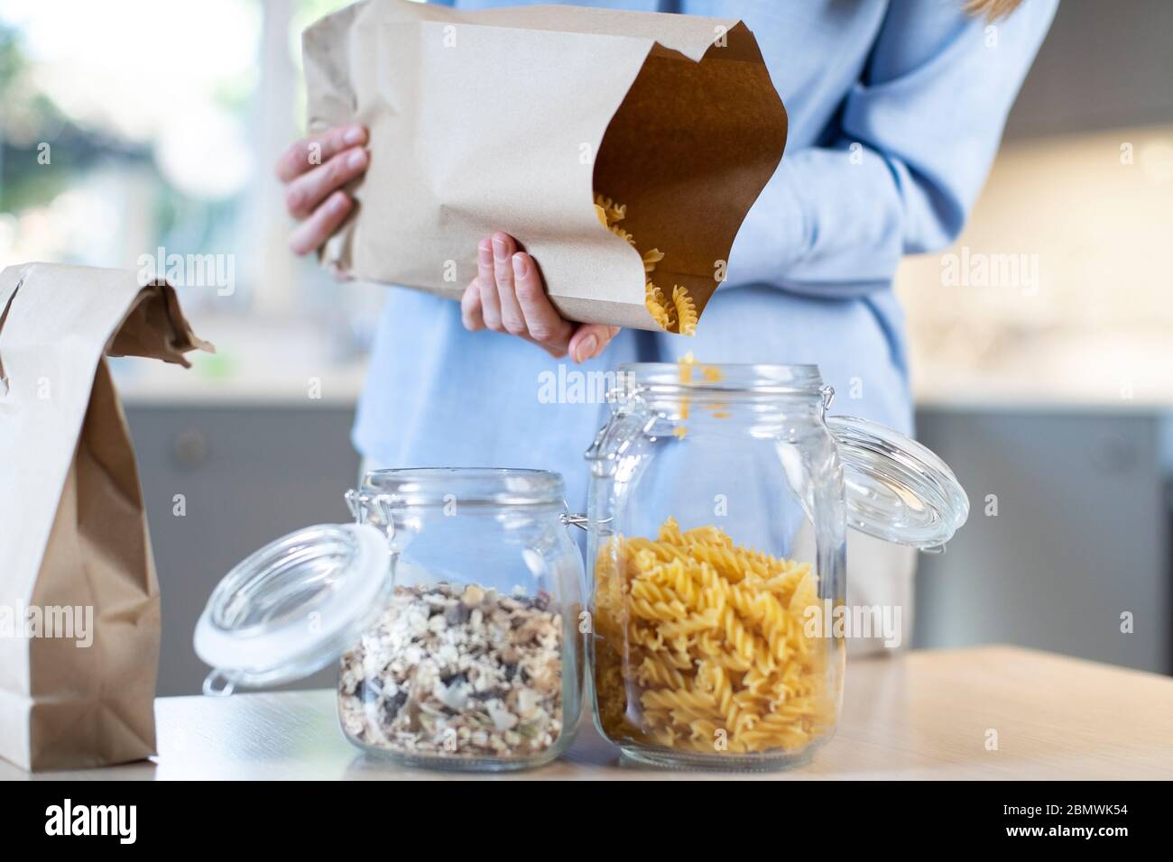 Close up donna versando la pasta a partire da plastica Free Packaging sacchetto di carta nella giara di storage Foto Stock