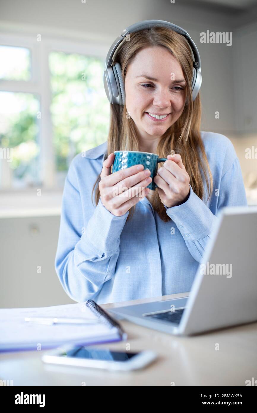 Donna che studiano a casa tramite laptop e indossa le cuffie Foto Stock
