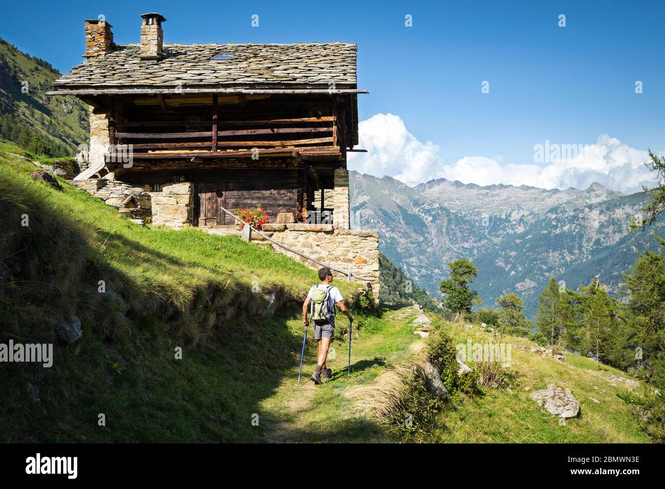 Trekking nelle Alpi in una bella giornata di sole su un sentiero panoramico con antica casa tradizionale Walser. Valle d'Aosta, Italia Foto Stock
