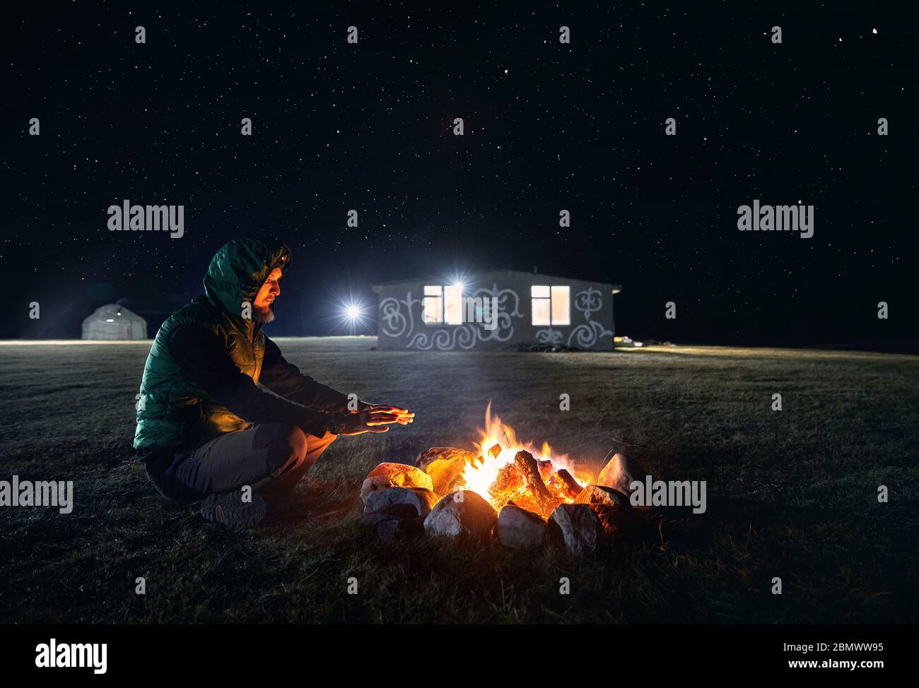 L uomo è seduto vicino a falò al campeggio nel borgo sotto il cielo notturno con stelle Foto Stock