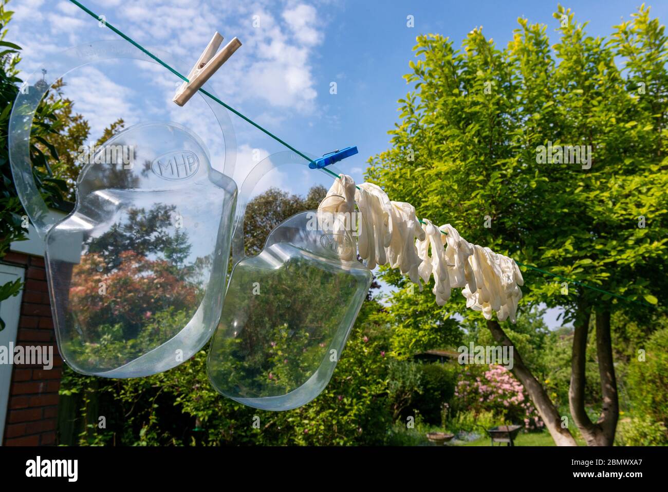 Maschere per coronavirus e guanti monouso che si asciugano sulla linea dei vestiti dopo essere stati lavati in candeggina e utilizzati Foto Stock