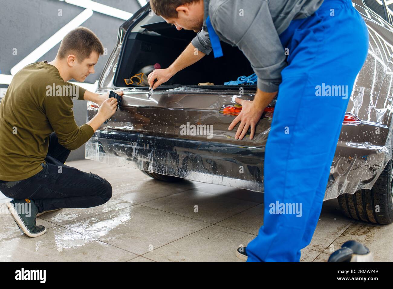 Gli specialisti applicano la pellicola di protezione dell'auto sul paraurti Foto Stock