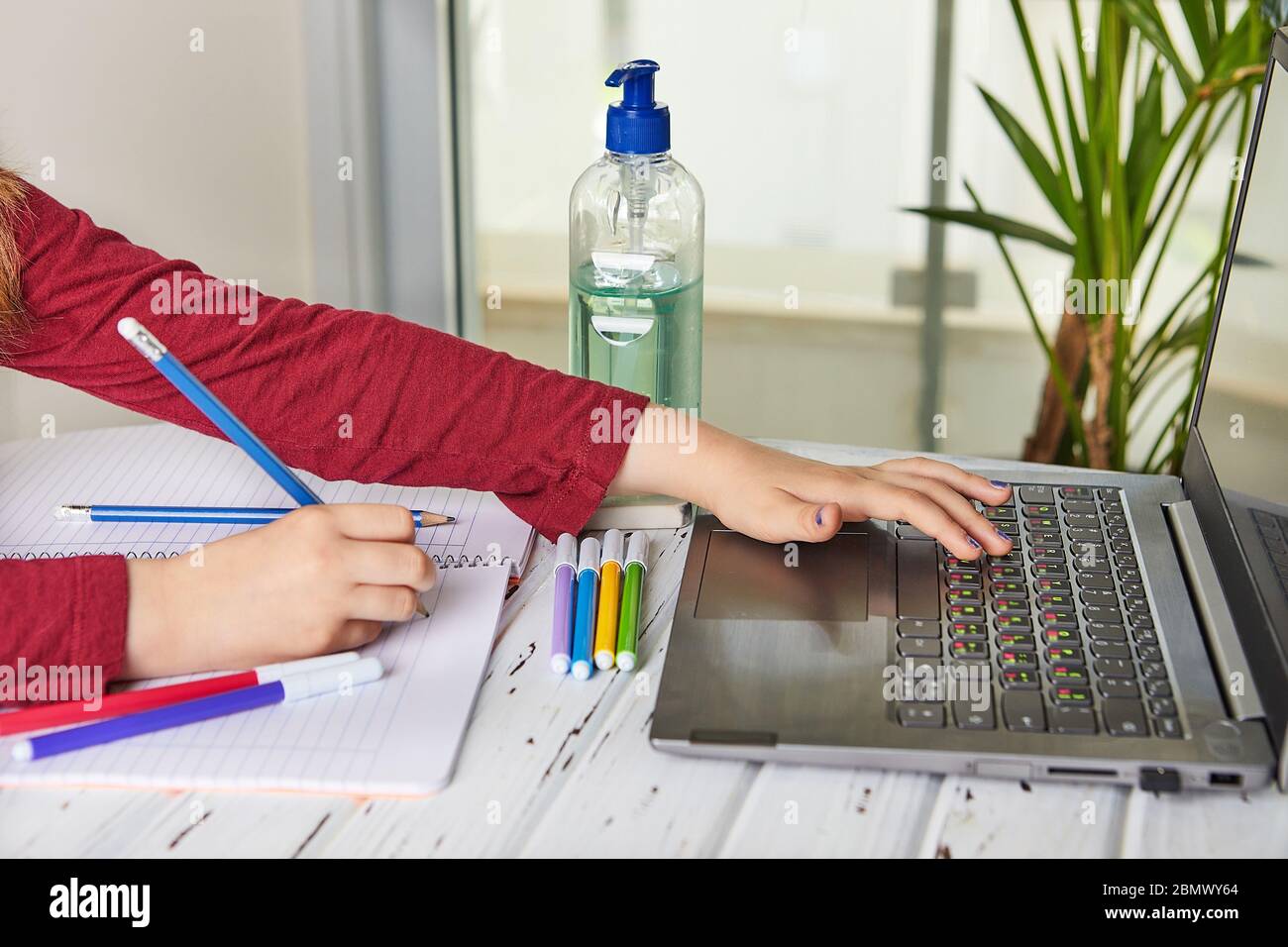 Formazione online a distanza. Studentessa studia a casa con un computer portatile e fa compiti a scuola. Libri di addestramento e penne colorate con punta in feltro Foto Stock