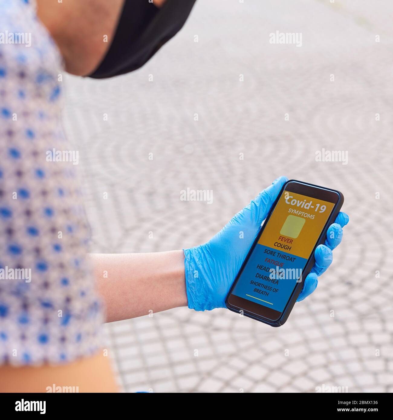 primo piano di un giovane caucasico sulla strada, indossando una maschera nera del viso e guanti blu in lattice, controllando alcuni dei sintomi del covid-19 in un si Foto Stock