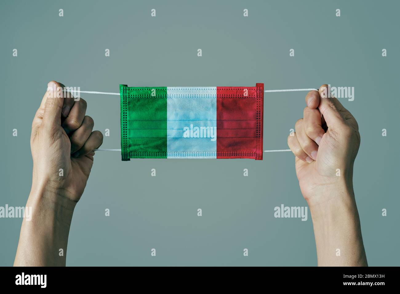 Primo piano di uomo con maschera chirurgica modellata con la bandiera italiana su sfondo grigio Foto Stock