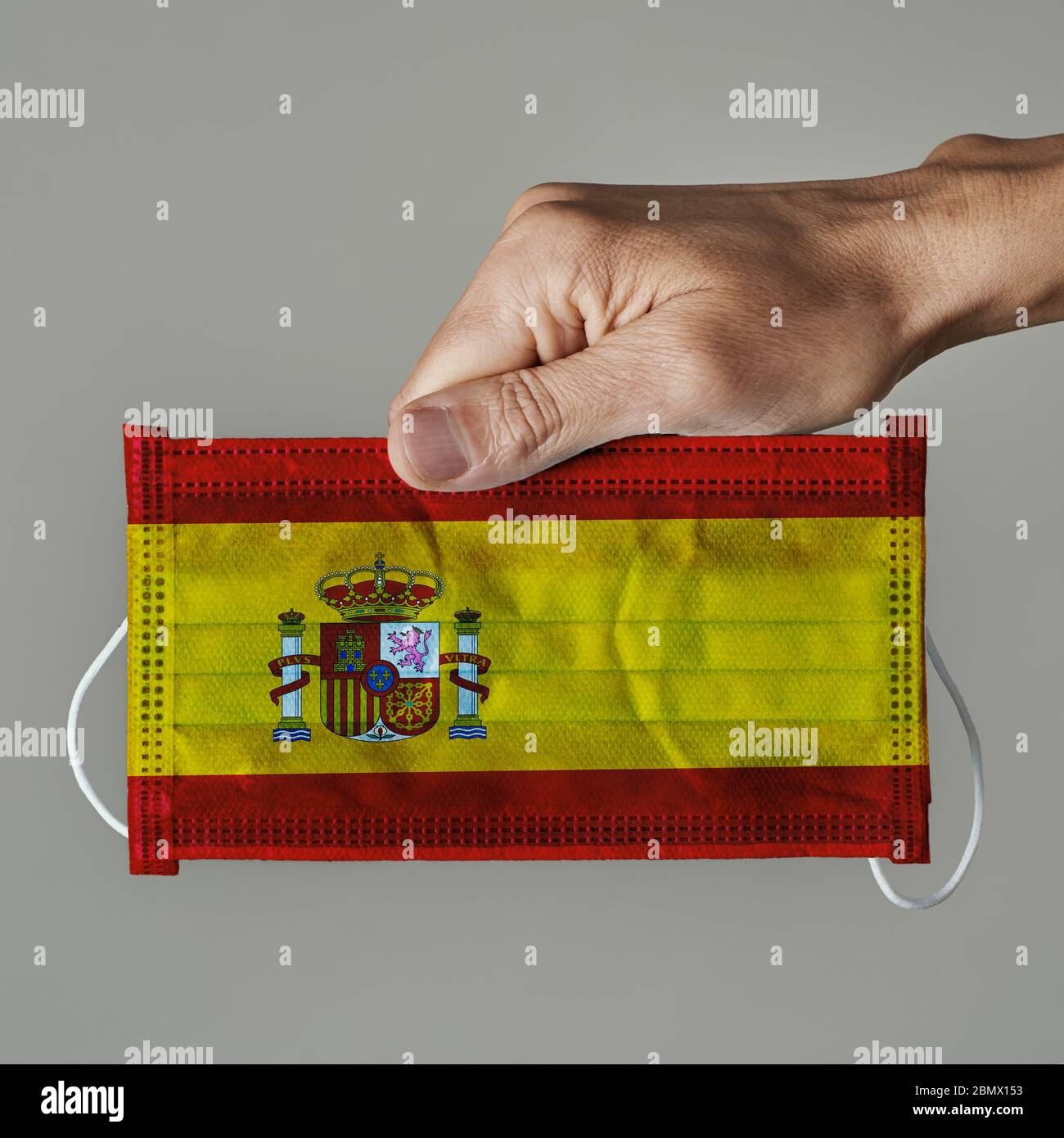 Primo piano di uomo con una maschera chirurgica modellata con la bandiera della Spagna su uno sfondo grigio Foto Stock