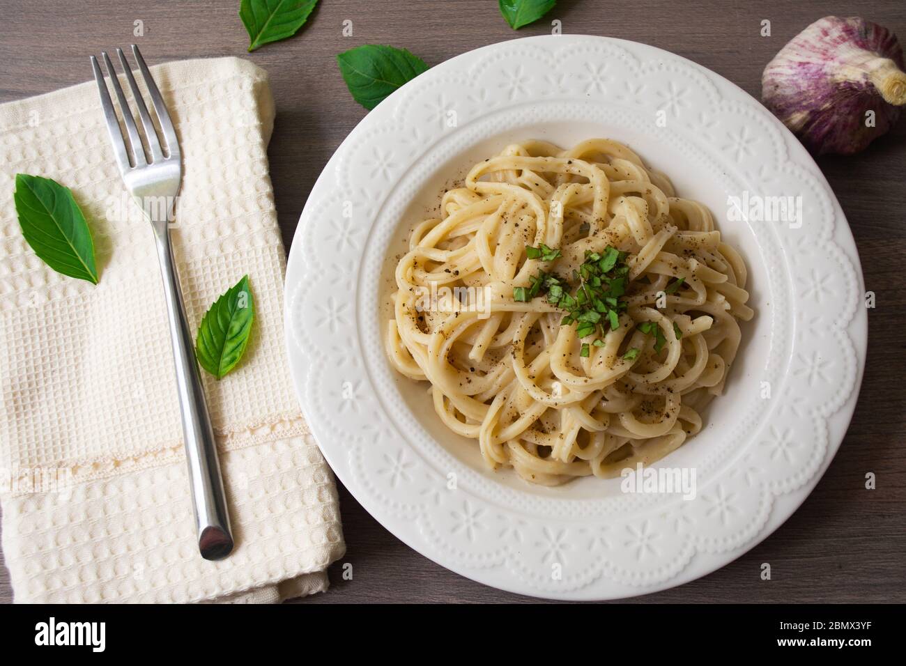 Versione vegana della tradizionale pasta italiana fettuccine alfredo con salsa bianca cremosa guarnita con basilico su una superficie di legno con forchetta, tovagliolo, ga Foto Stock
