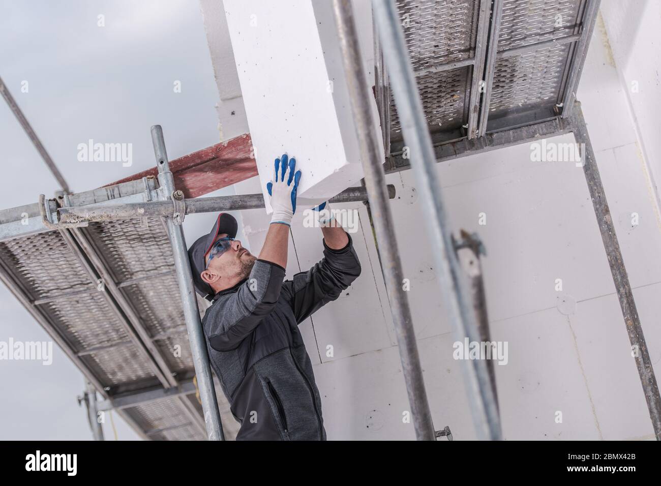 Addetto alla costruzione maschio caucasico che installa pannelli di schiuma isolante all'esterno dell'edificio. Foto Stock