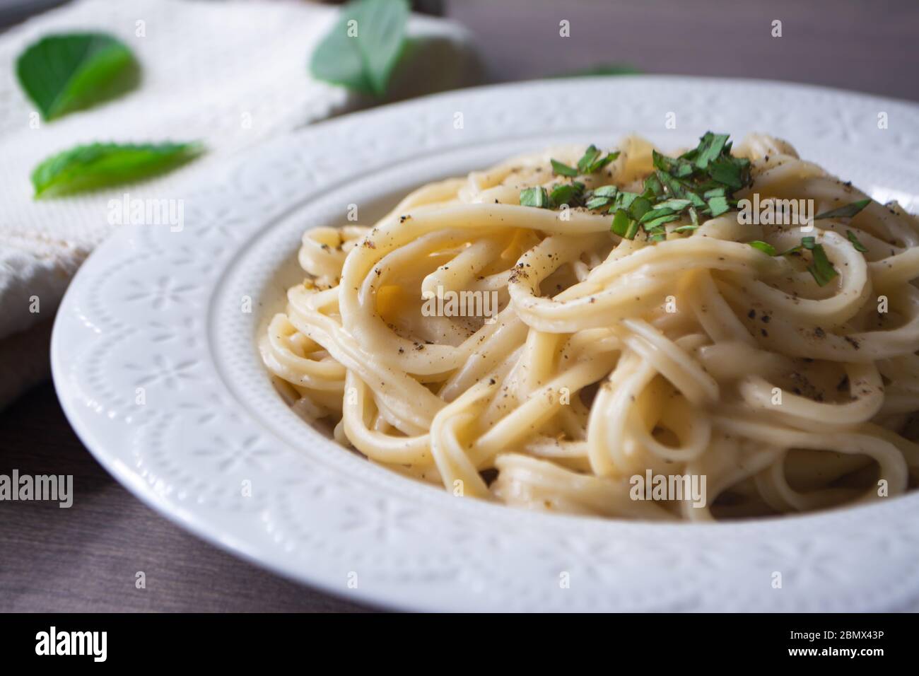 Versione vegana della tradizionale pasta italiana fettuccine alfredo con salsa bianca cremosa guarnita con basilico su una superficie di legno con forchetta, tovagliolo, ga Foto Stock