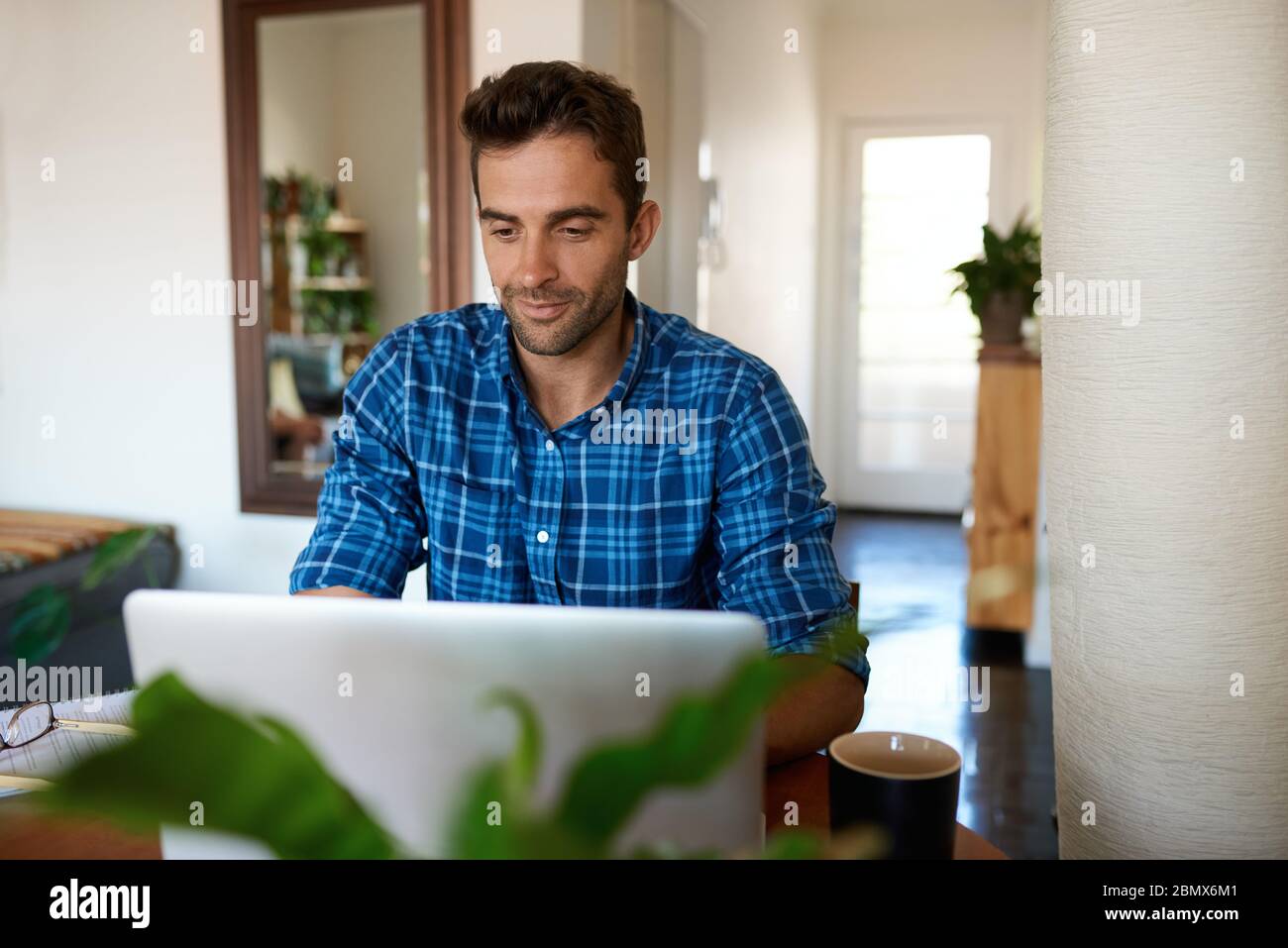 Giovane uomo che lavora online con un computer portatile nel suo appartamento Foto Stock