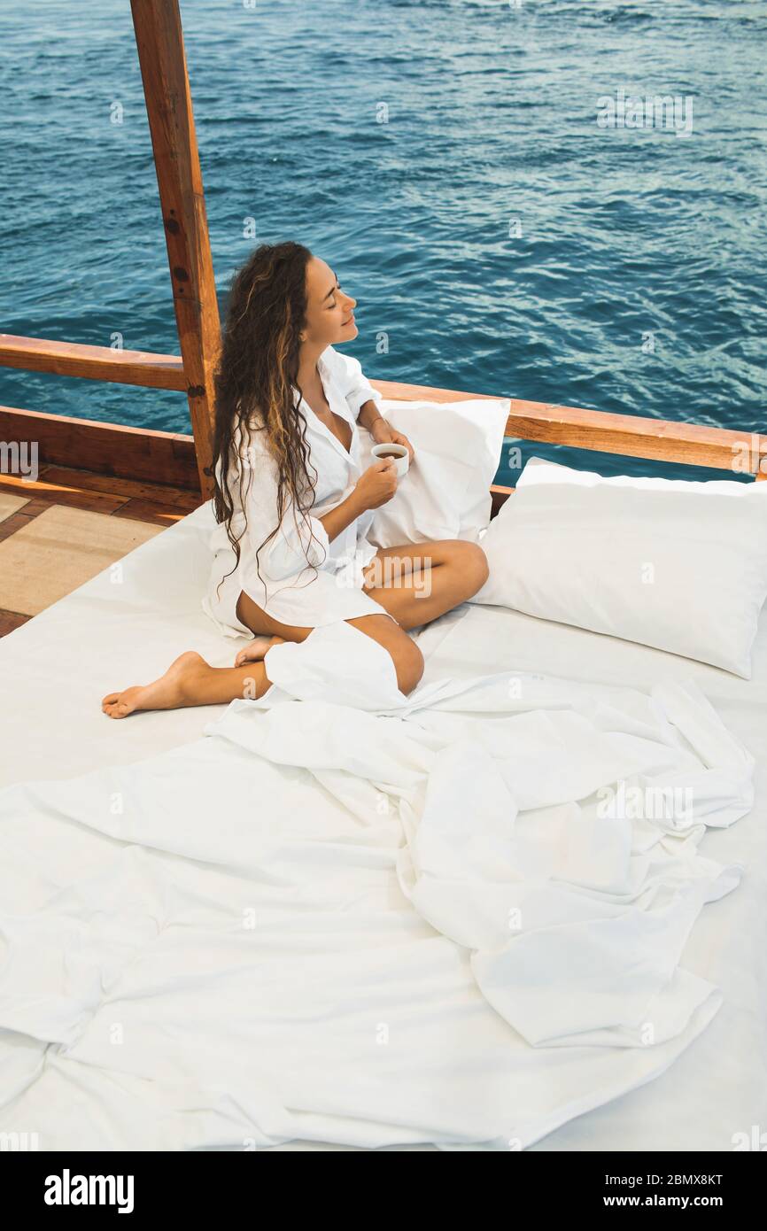 La donna si risveglia e si gusta il caffè mattutino in barca con un tour privato in crociera. Letto a bordo. Viaggi e libertà di stile di vita. Foto Stock
