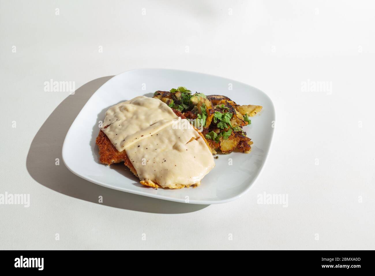 Schnitzel con formaggio al gratin con patate fritte su un piatto bianco-isolato su bianco Foto Stock