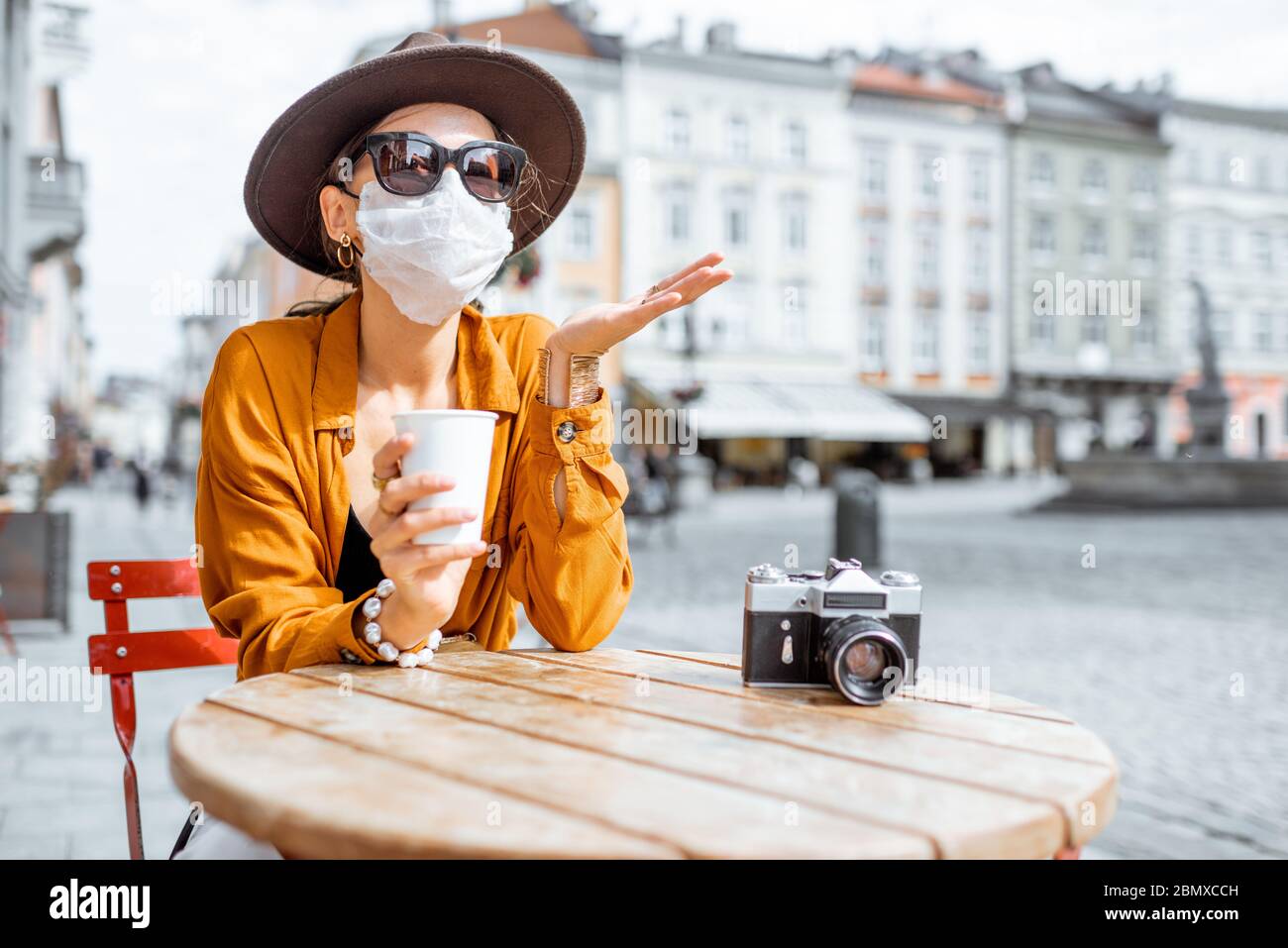 Donna disaccoppiata in maschera facciale seduta sulla terrazza del caffè da sola. Concetto di distanza sociale e nuove regole sociali dopo la pandemia di coronavirus. Foto Stock