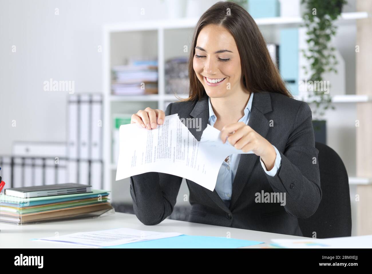 Buona donna esecutiva che rompe il documento del contratto seduto su una scrivania in ufficio Foto Stock
