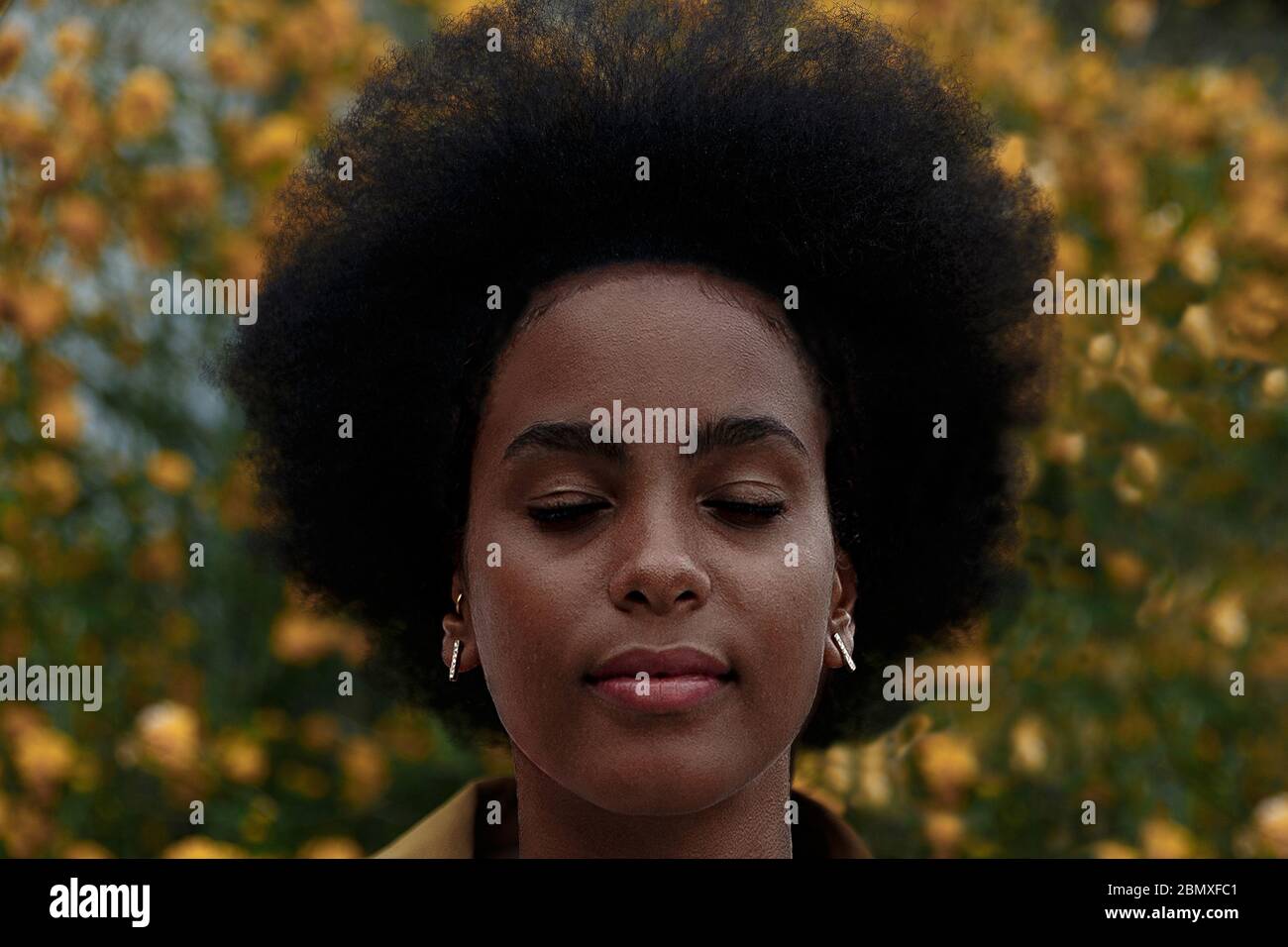 donna afro pensierosa con occhi chiusi in un giardino Foto Stock