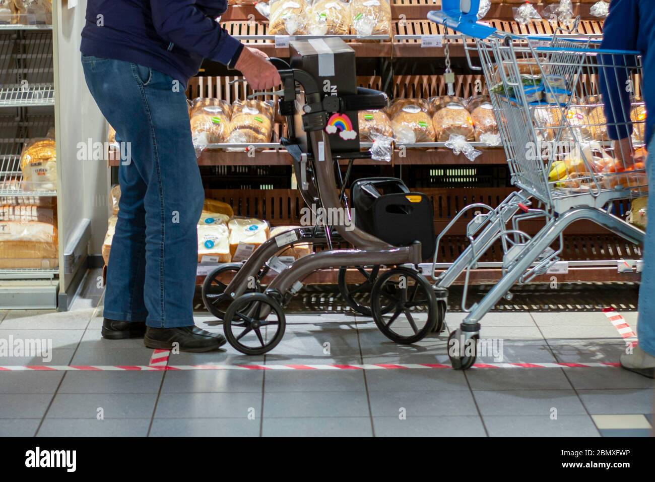 Uomo anziano che fa generi alimentari insieme in un supermercato durante la pandemia di coronavirus covid-19. Il nastro a terra indica la distanza sociale di sicurezza Foto Stock